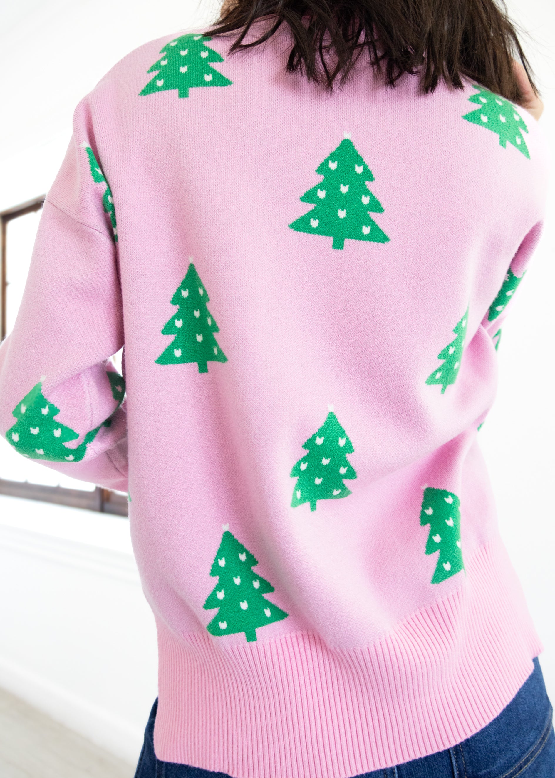 Pink sweater with green tree patterns worn by a person