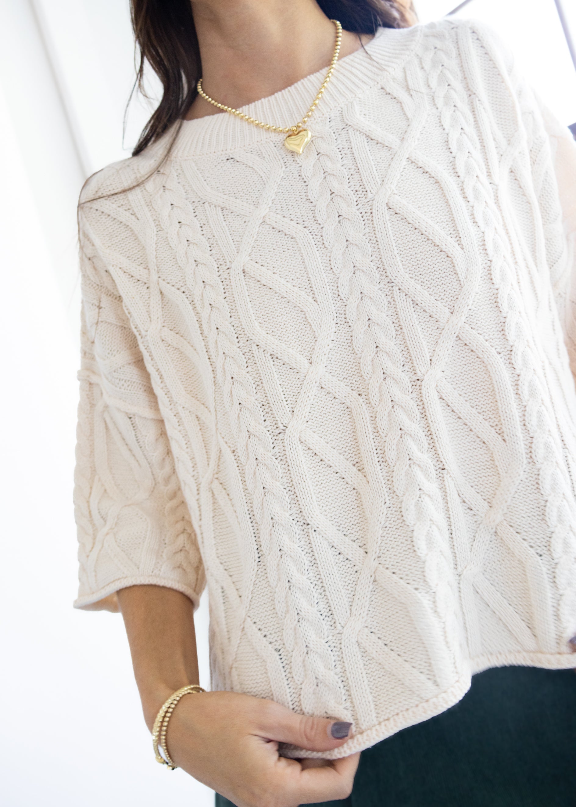 Close-up of a person wearing a white cable knit sweater with a blurred background