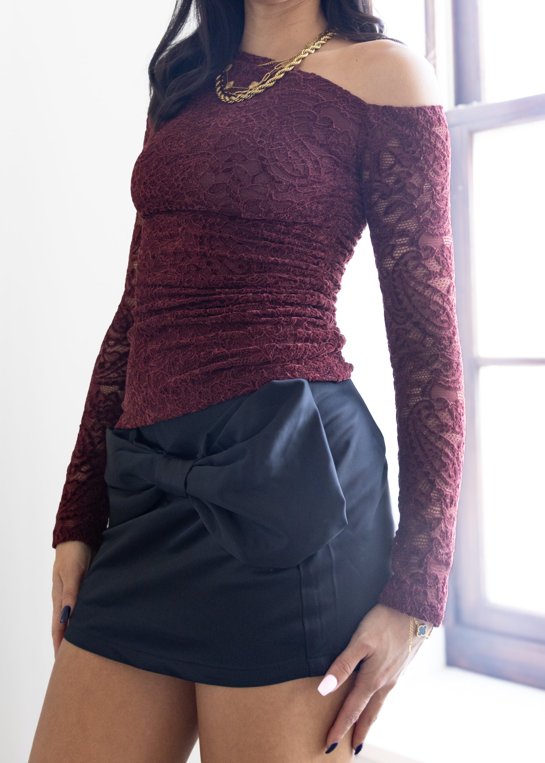 Person wearing a maroon lace top and black skirt in front of a window.