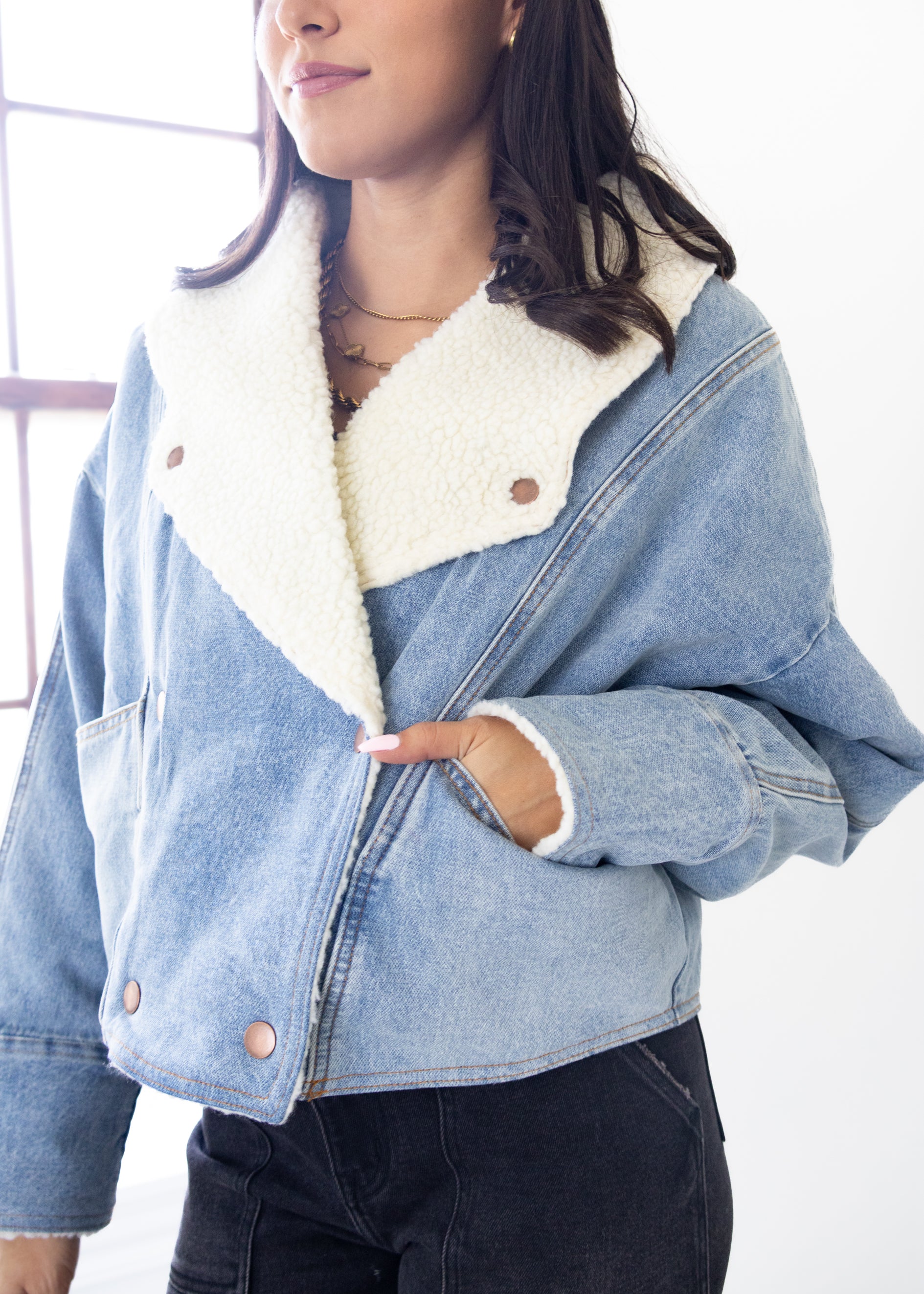 Denim jacket with white fur lining worn by a person indoors.
