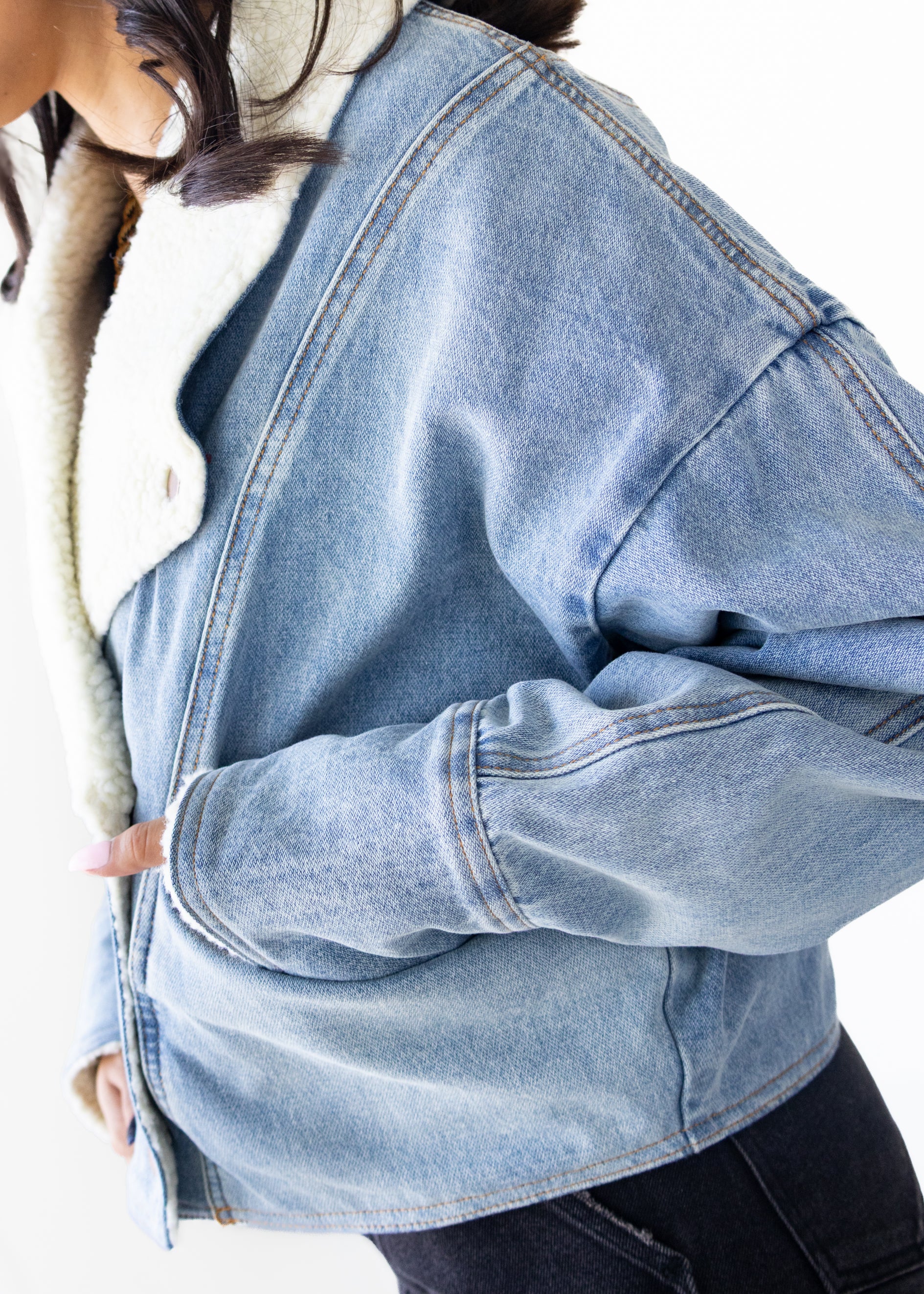 Close-up of a person wearing a light blue denim jacket on a white background