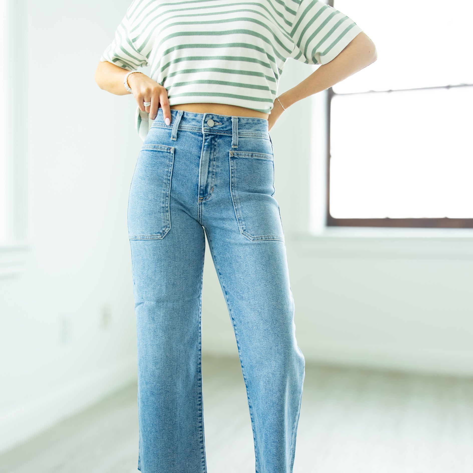 Person wearing a striped shirt and blue jeans in a minimalistic room.