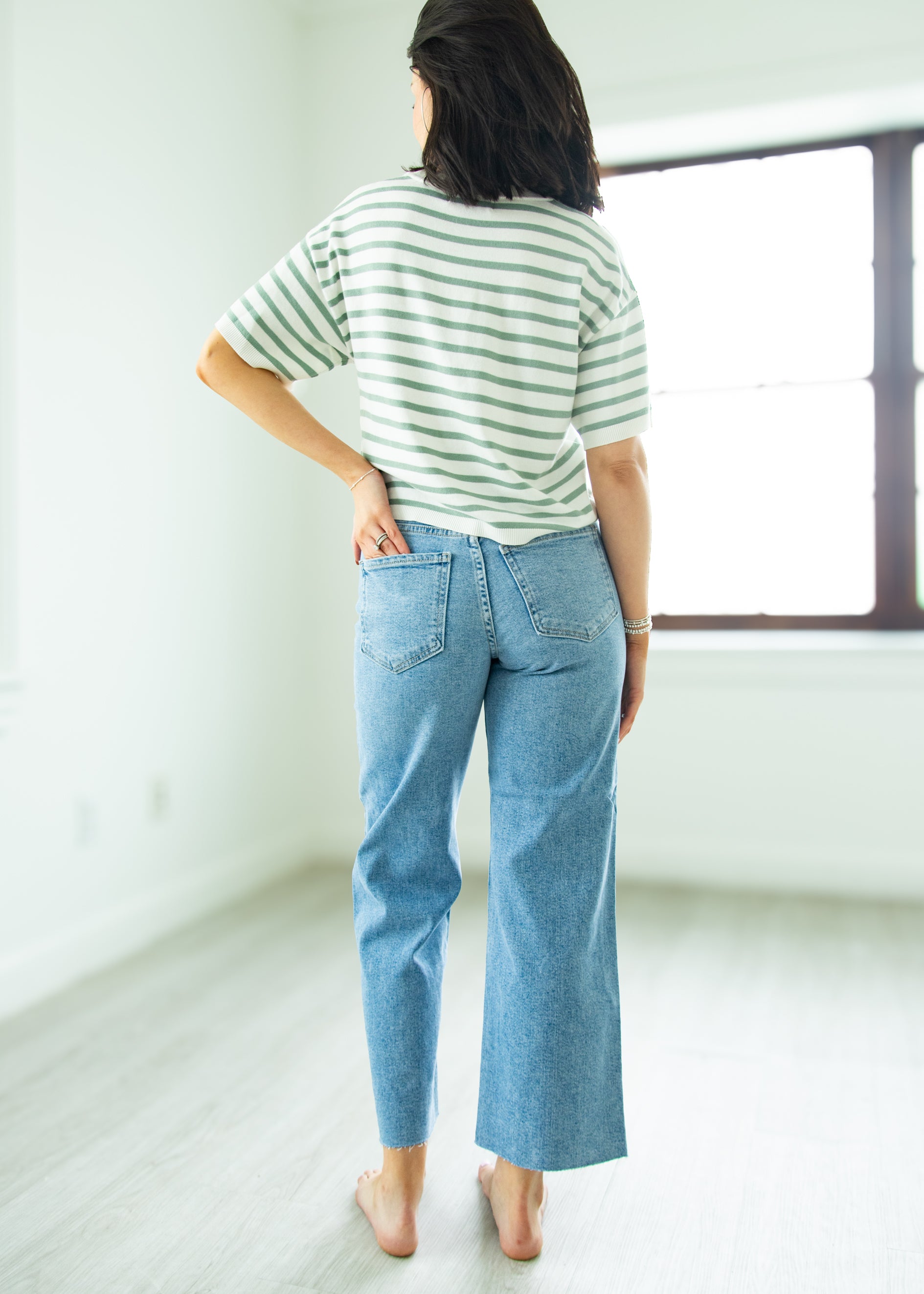 Person wearing a striped shirt and blue jeans standing in a minimalistic room.