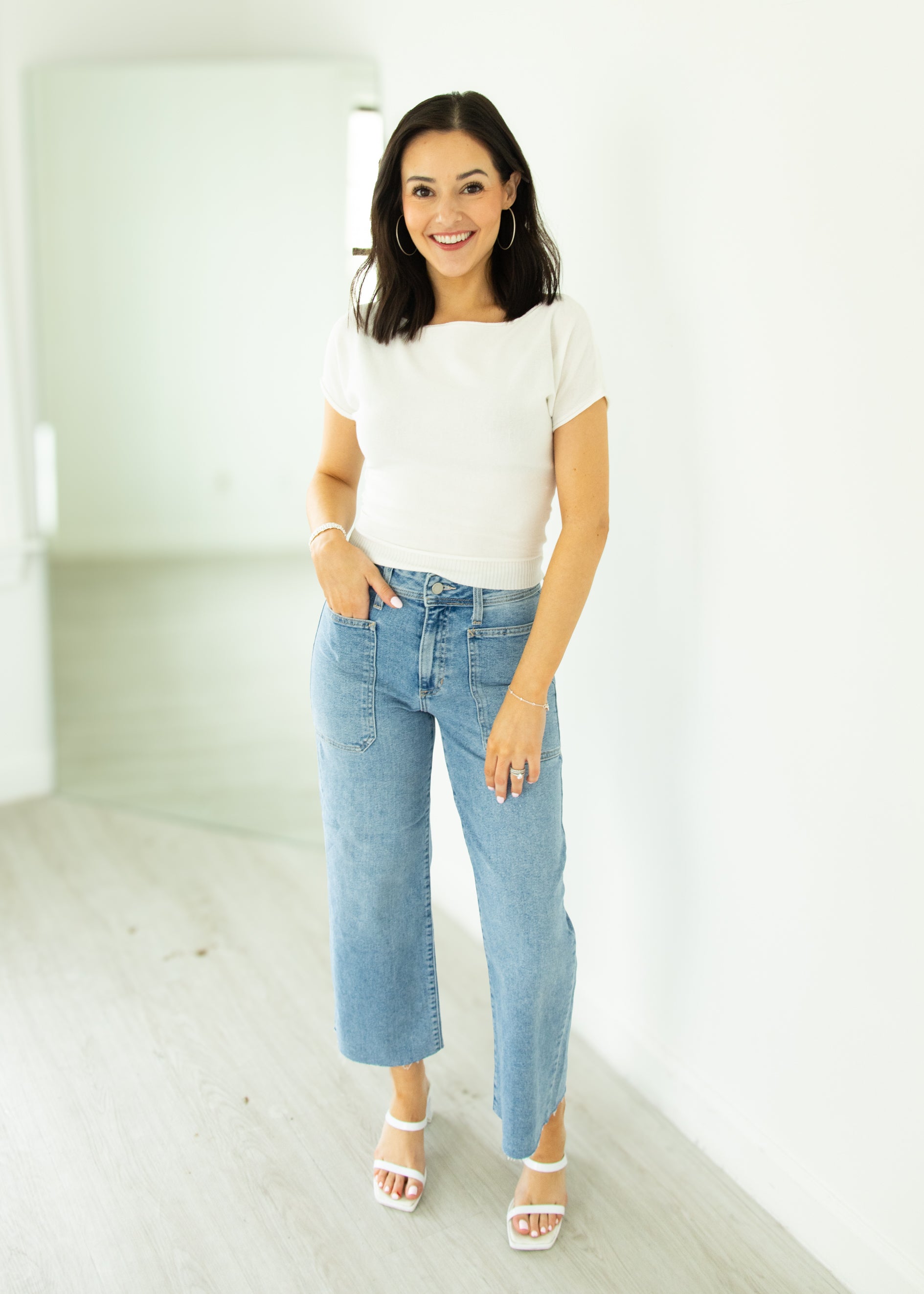 Woman wearing a white t-shirt and blue jeans standing in a minimalistic room.