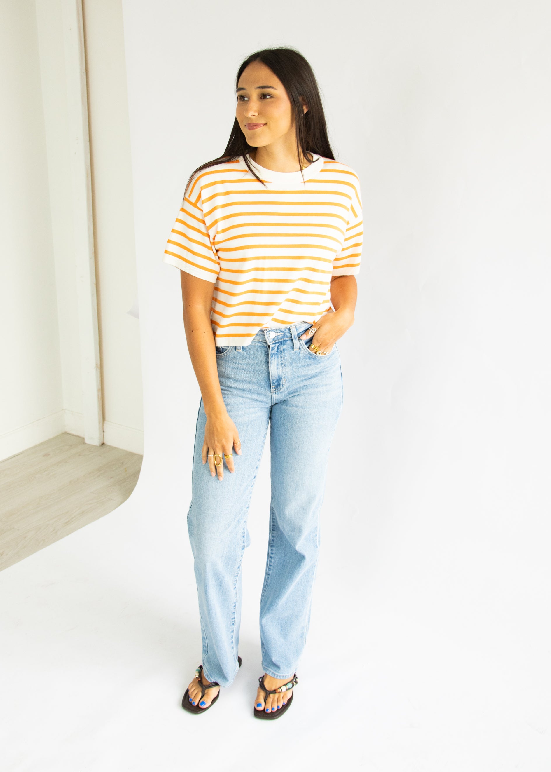 Woman wearing a striped shirt and light blue jeans against a white background