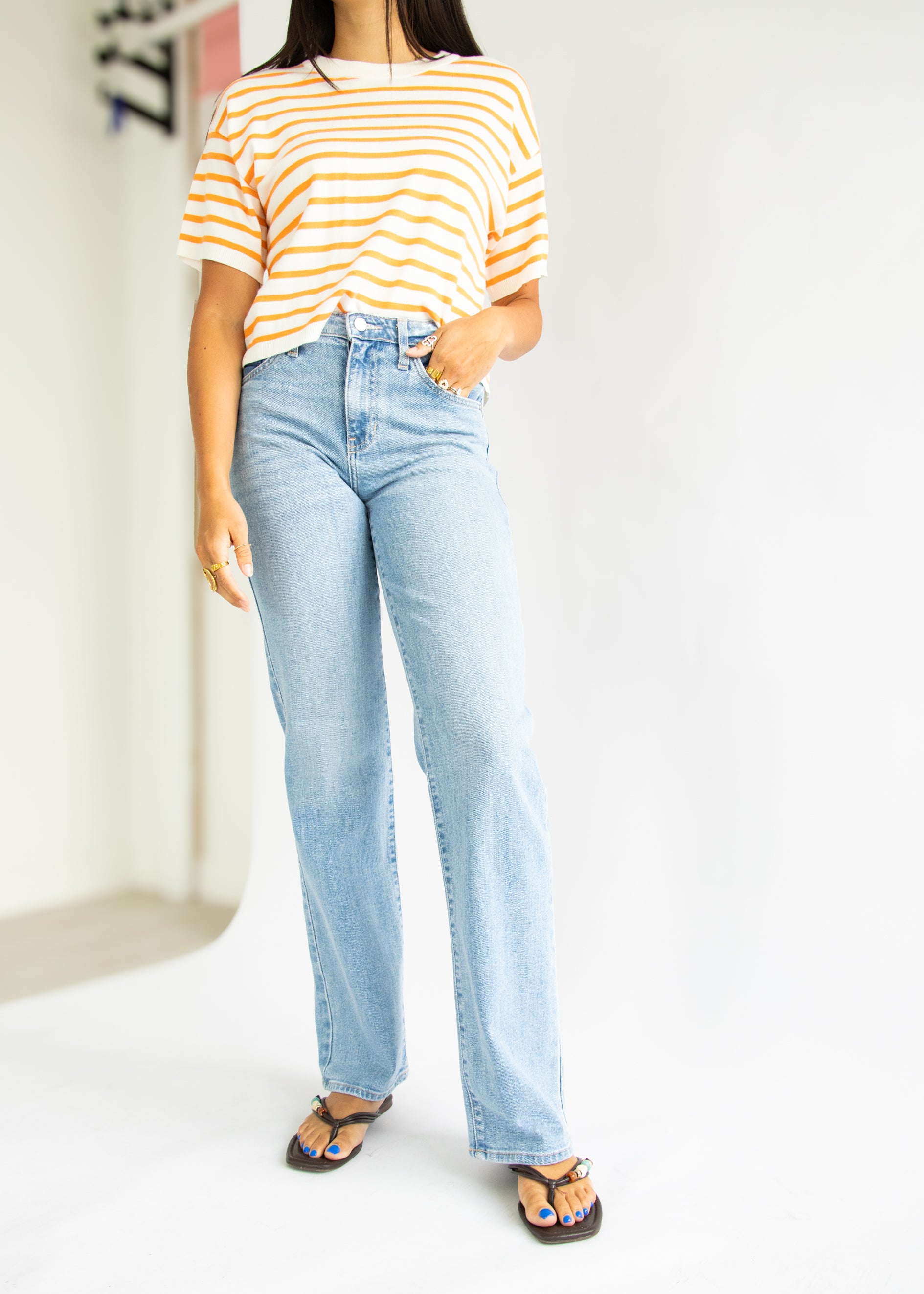 Person wearing a striped shirt and light blue jeans on a white background