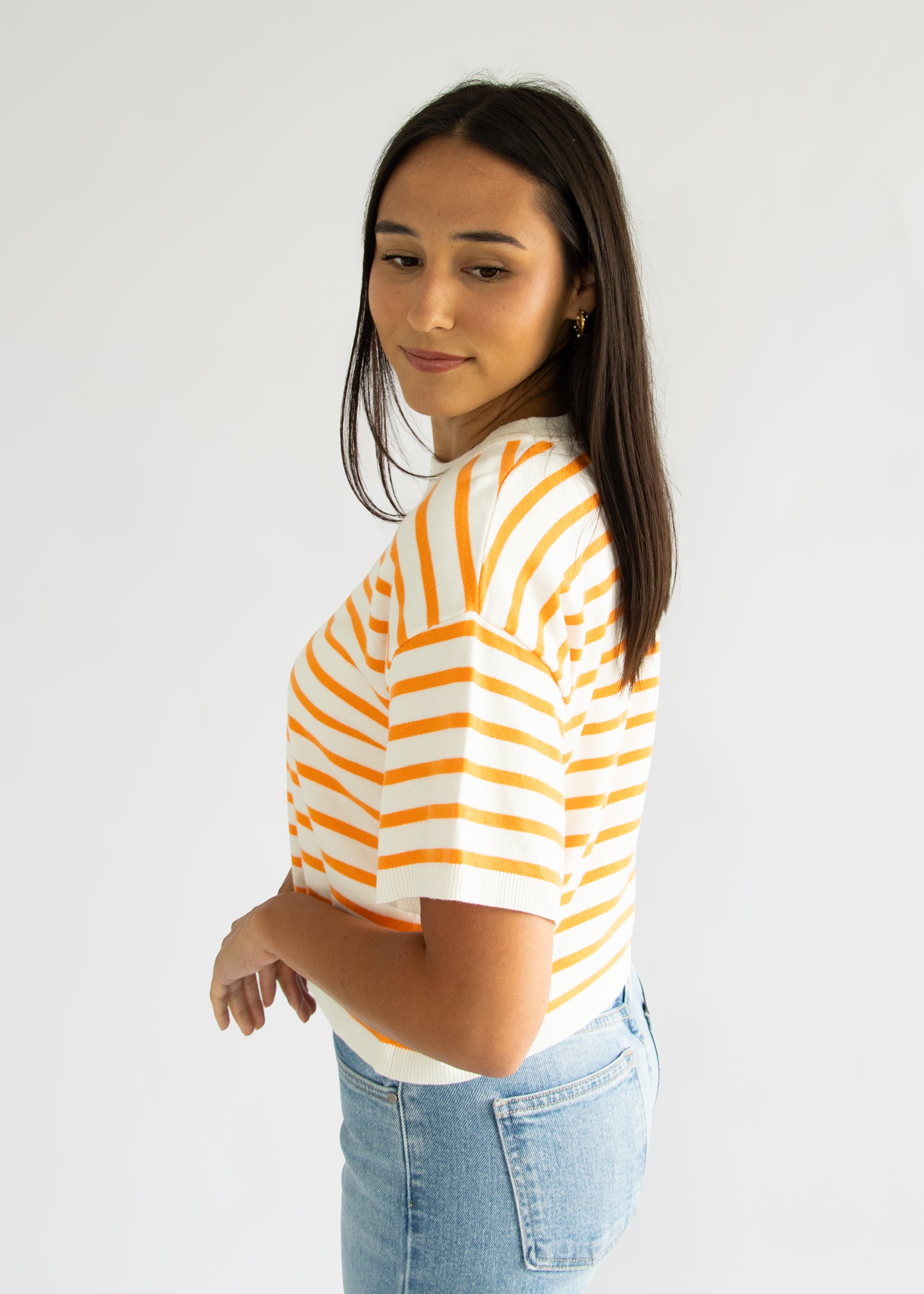 Woman wearing a yellow and white striped shirt with blue jeans on a plain background