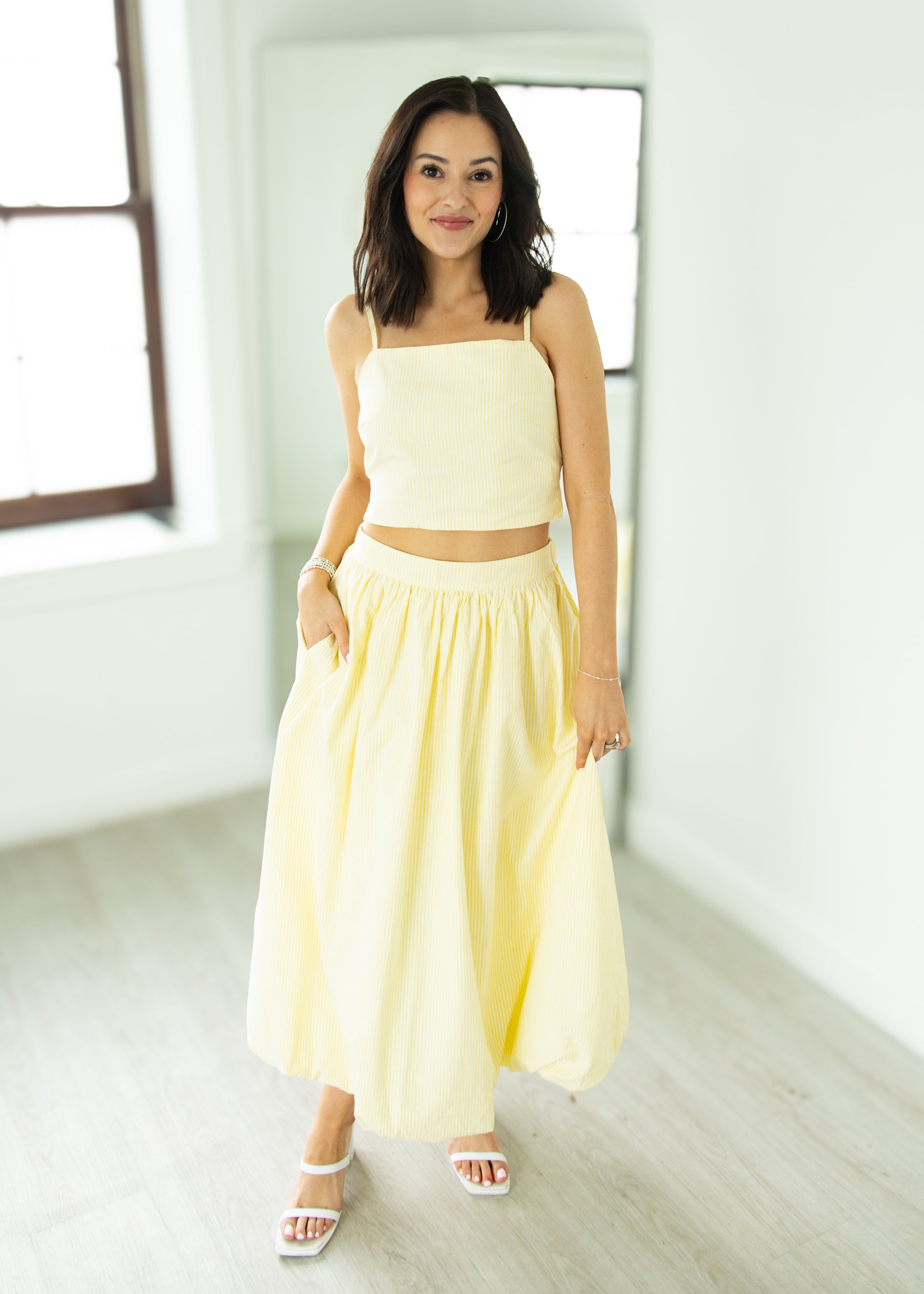 Woman wearing a yellow outfit standing in a bright room with large windows.