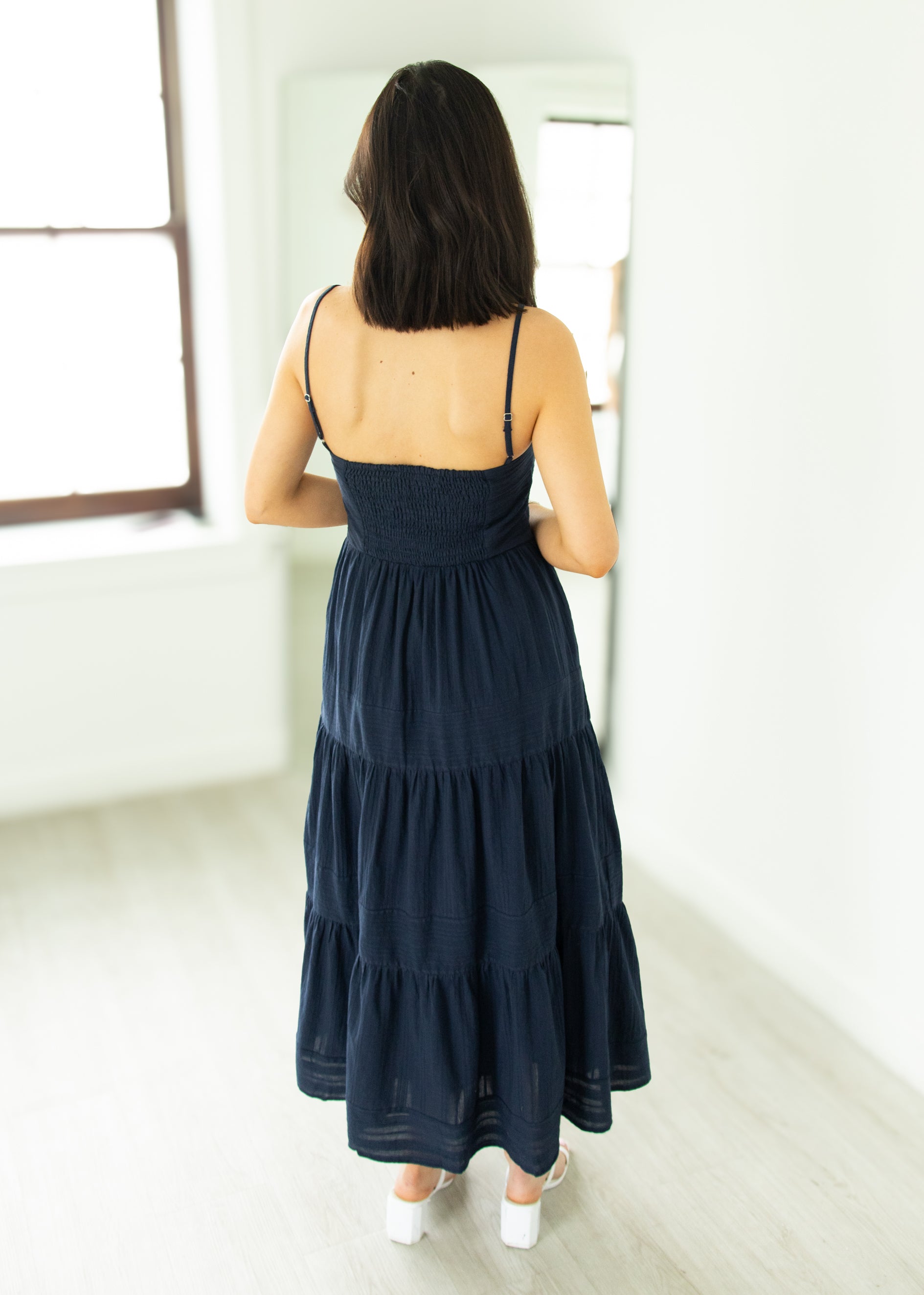 Woman wearing a navy blue dress standing in a room with a window.