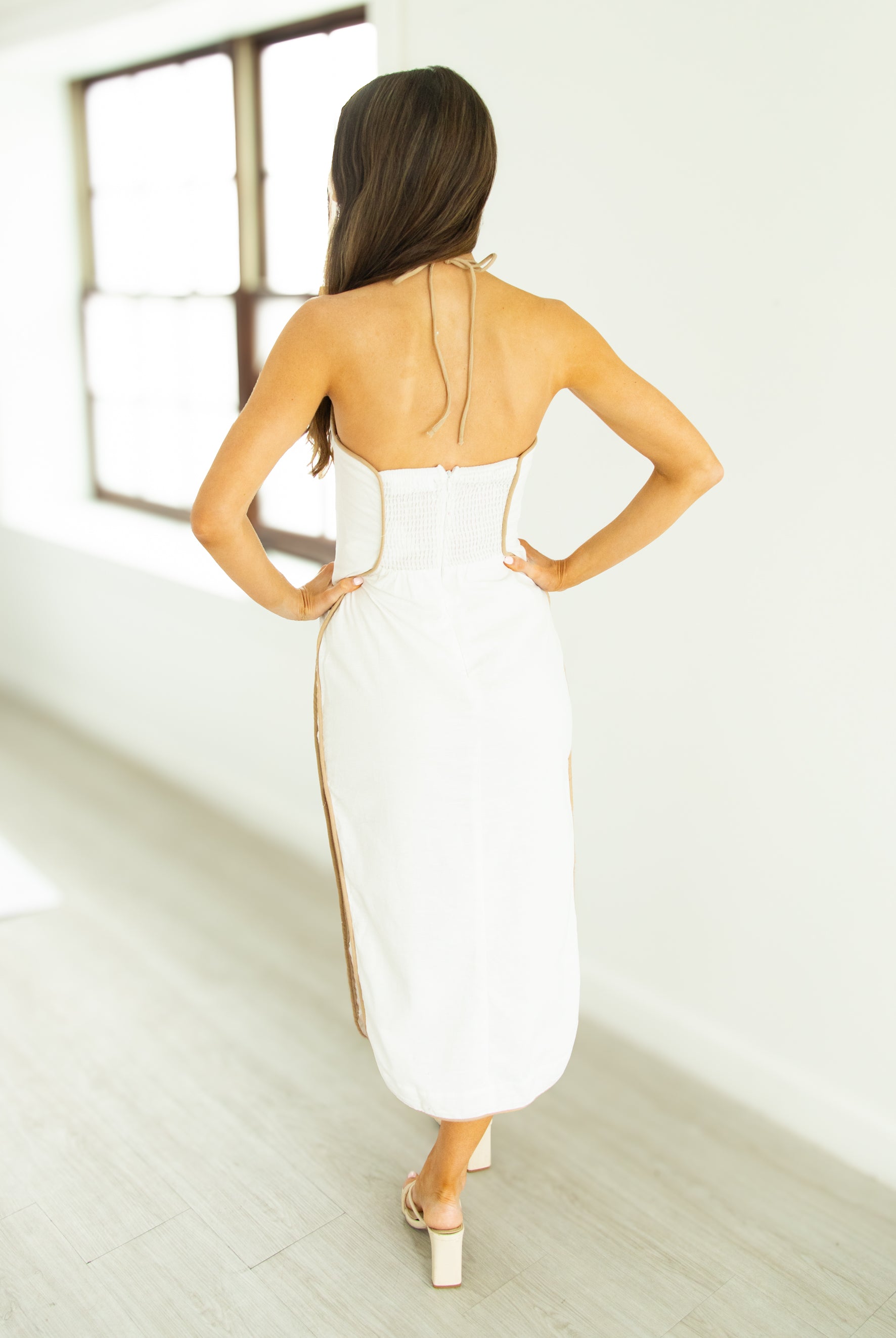 Woman in a white dress with gold accents standing in a minimalistic room.
