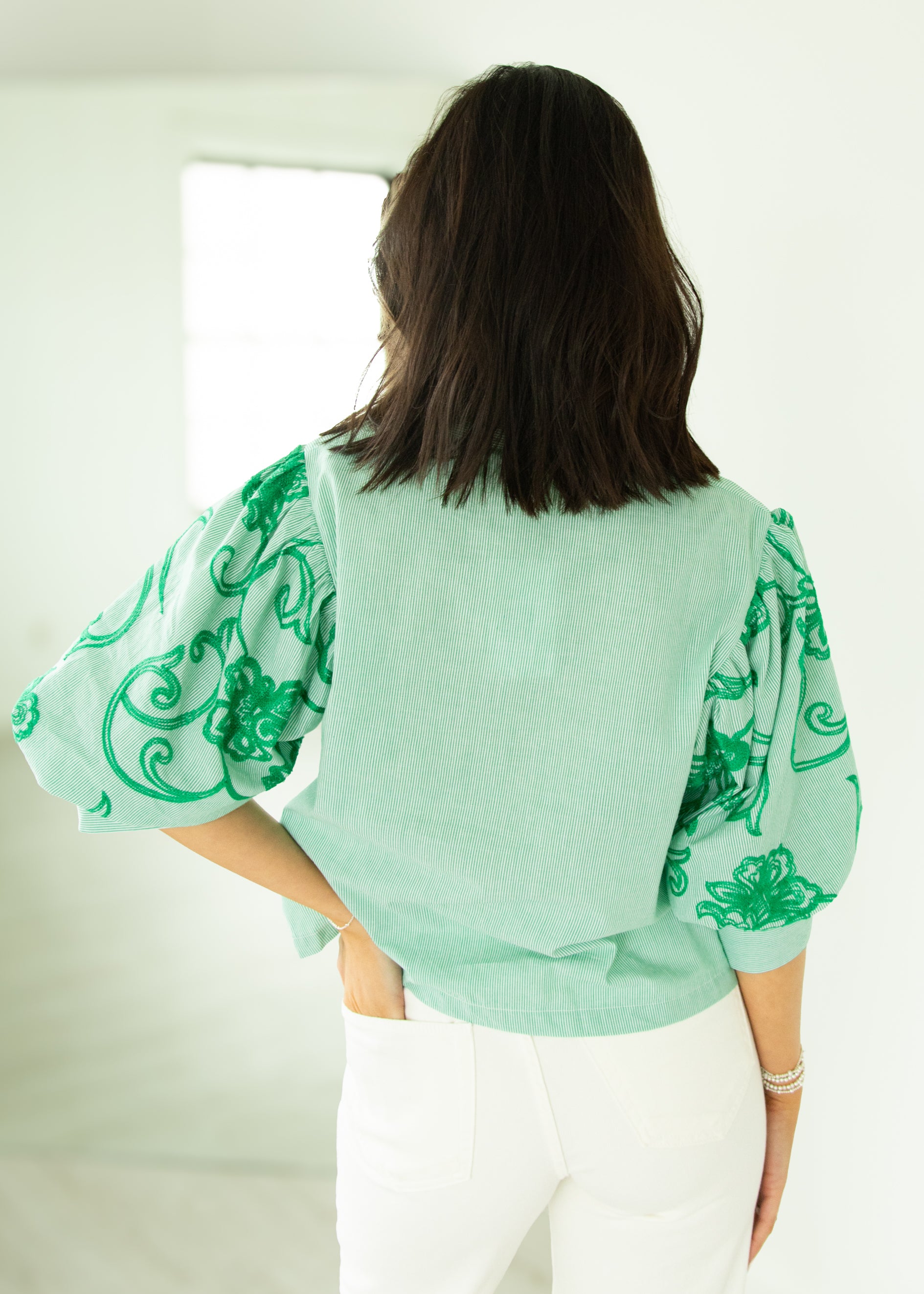 Person wearing a light green blouse with green patterns in a minimal indoor setting