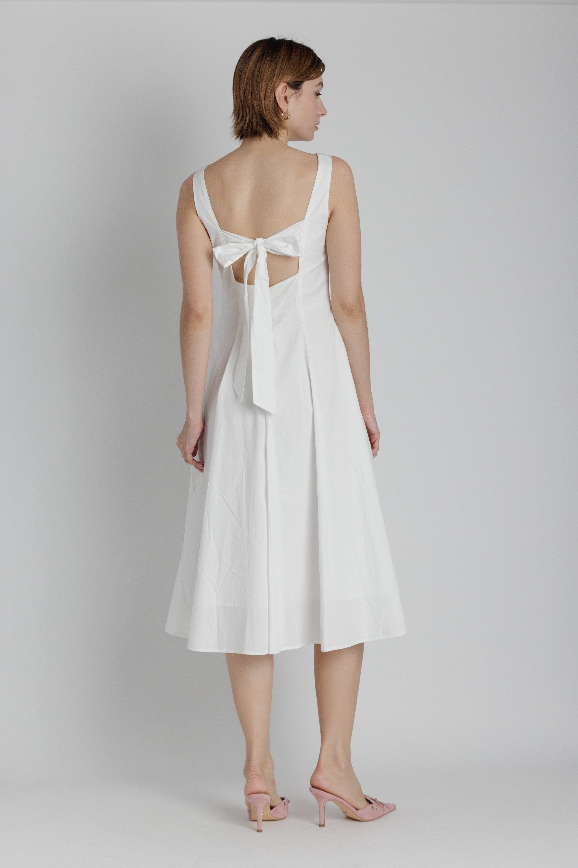 Woman wearing a white dress with cut-out back design on a plain background