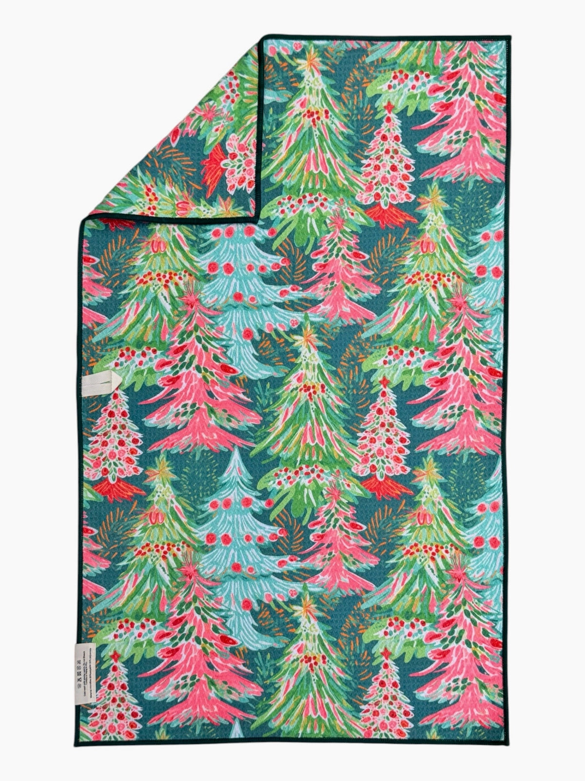 A folded rectangular towel or blanket with a festive Christmas tree pattern, featuring pink, green, and light blue trees on a dark teal background, with a black border.