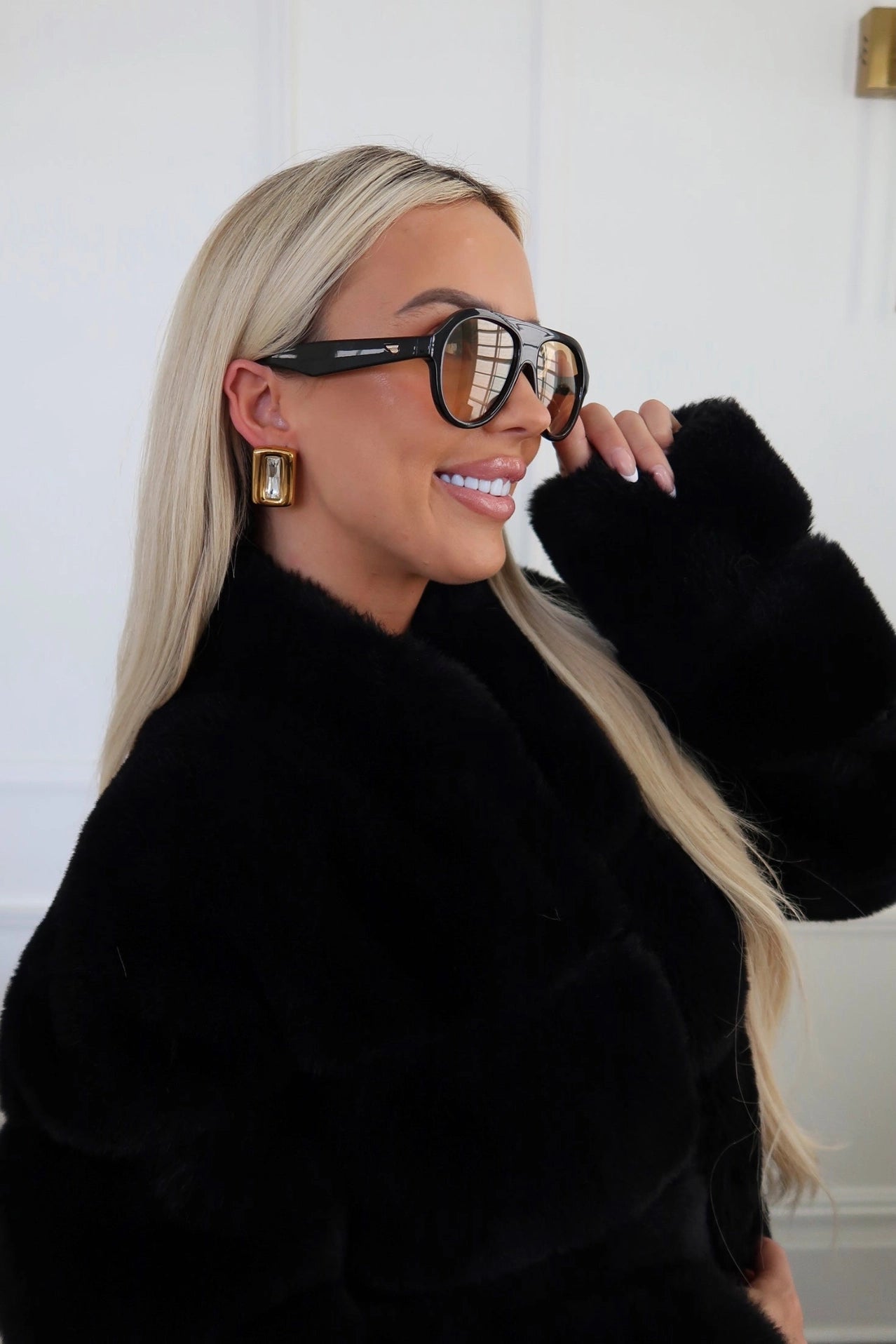 Woman wearing a black fur coat and large sunglasses indoors.