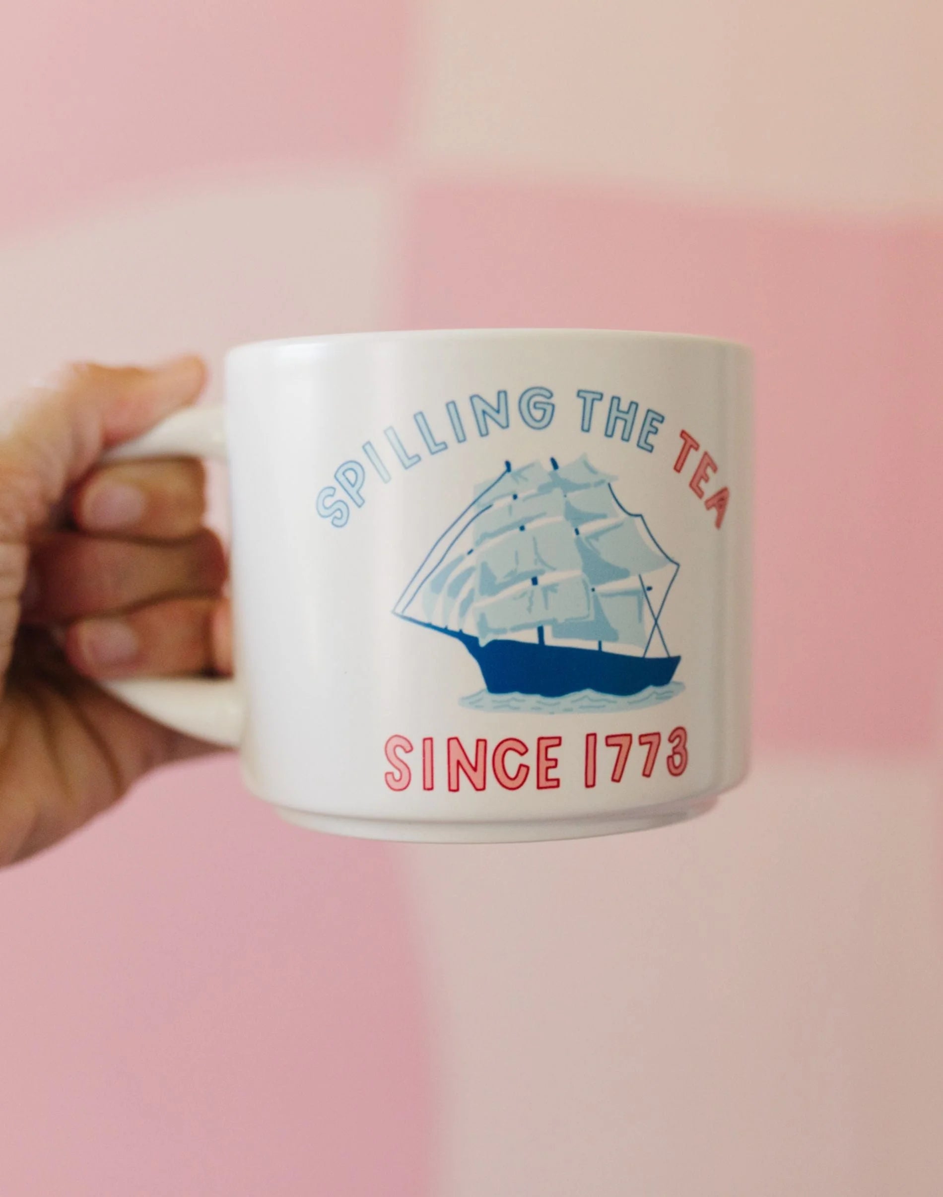 Mug with ship design and text 'Spilling the Tea Since 1773' held against a pink background