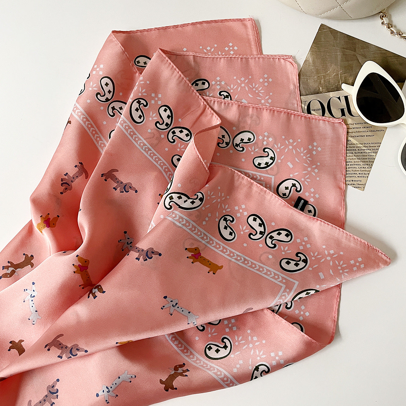 Set of pink patterned handkerchiefs on a white surface with sunglasses and a magazine.
