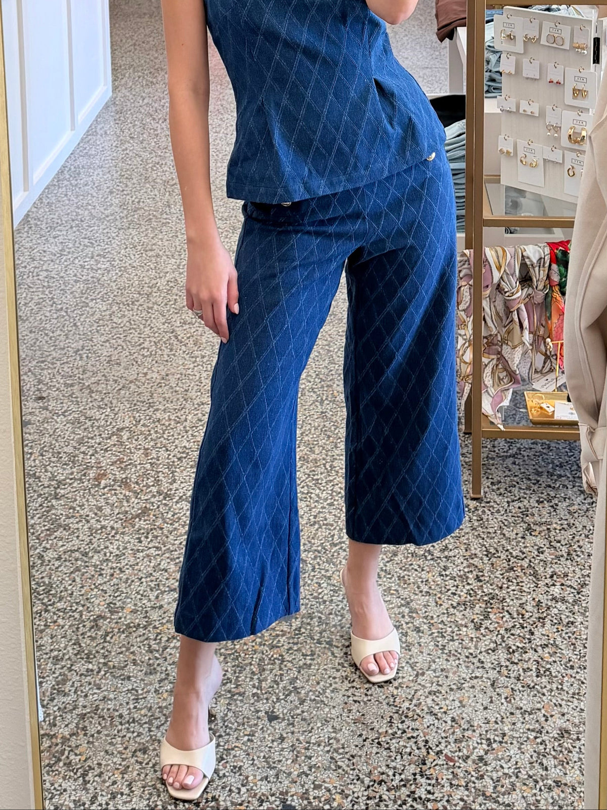 A woman takes a mirror selfie in a boutique wearing a matching blue patterned two-piece set consisting of a sleeveless peplum top and wide-leg cropped pants.