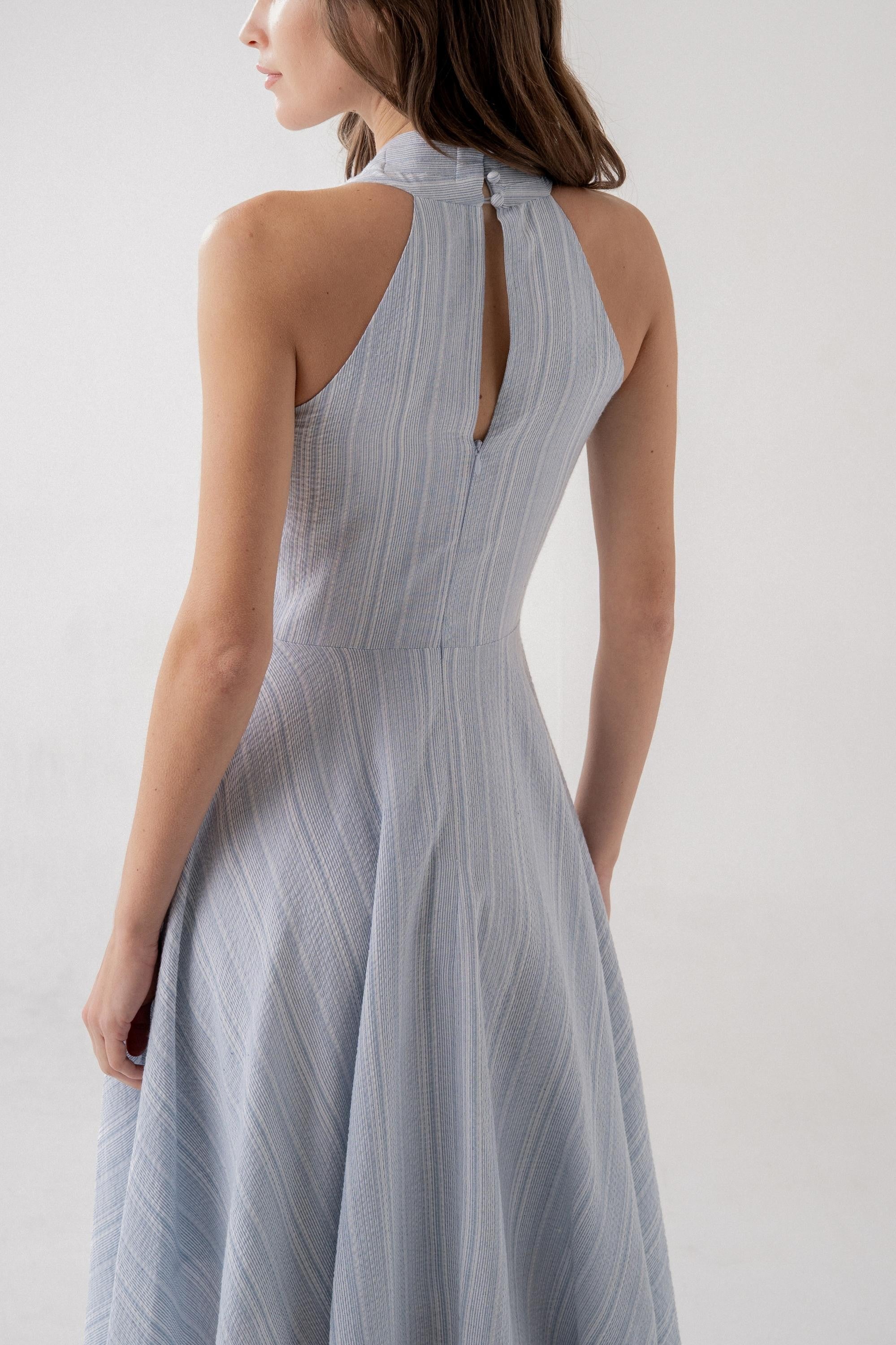 Woman wearing a light blue halter neck dress against a white background