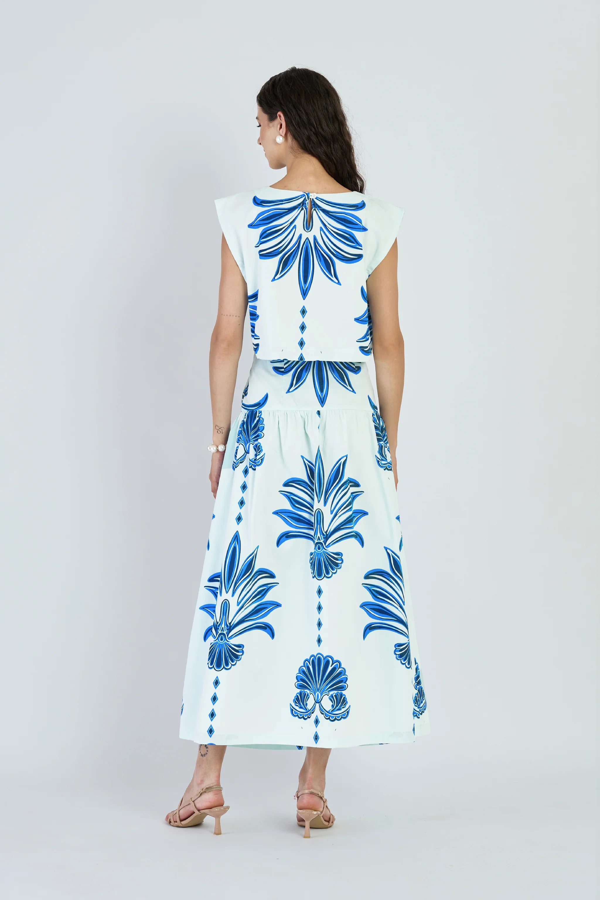Woman wearing a white dress with blue floral patterns on a plain background
