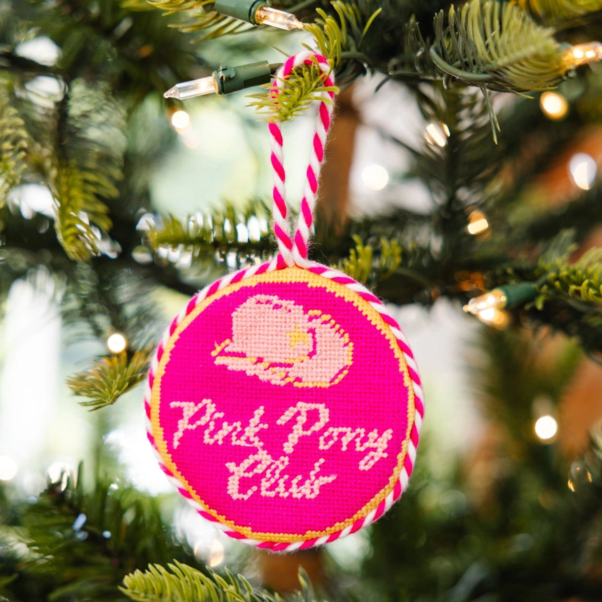 Pink round ornament with 'Pink Pony Club' text and logo on a Christmas tree.