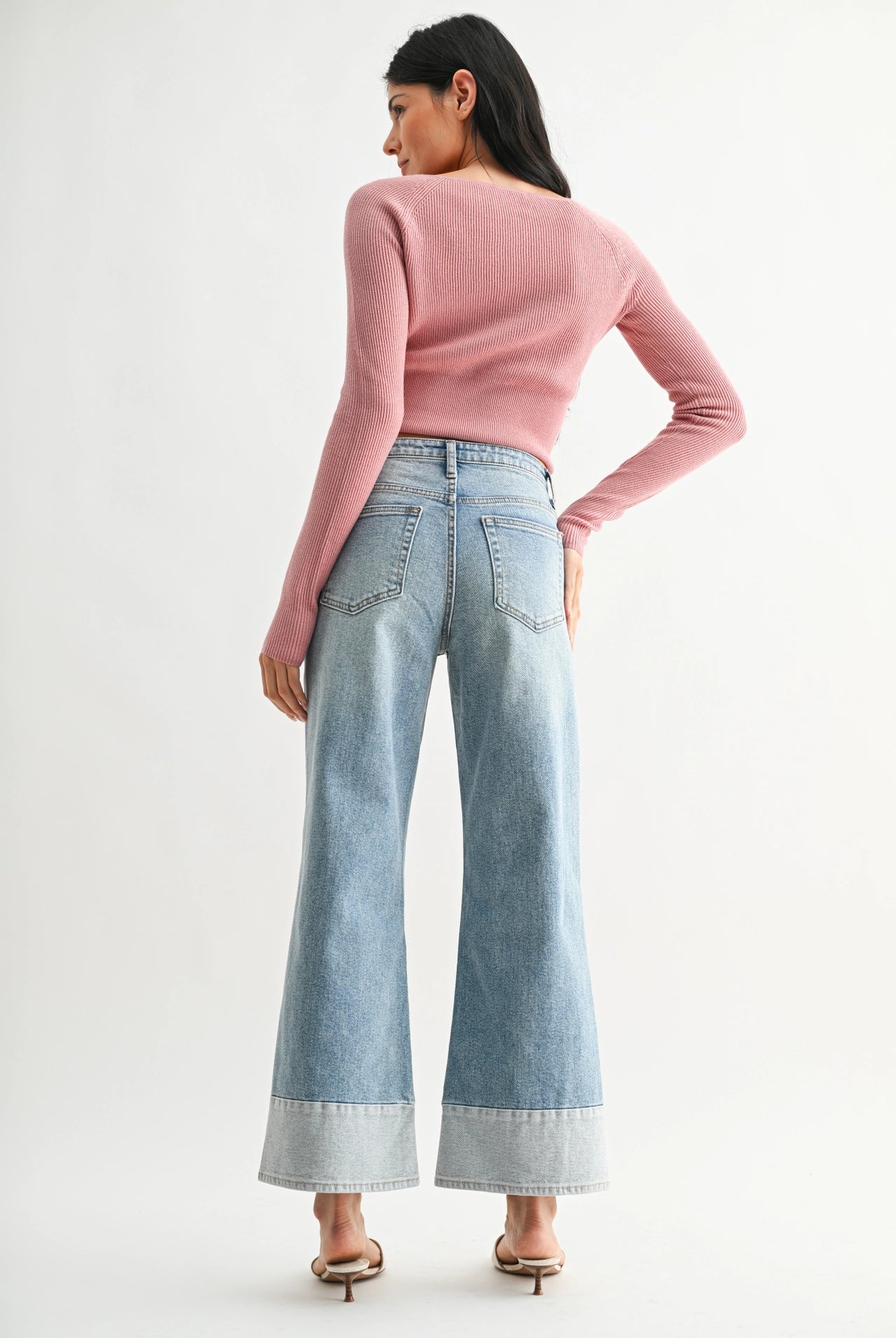Woman wearing a pink sweater and light blue jeans on a white background