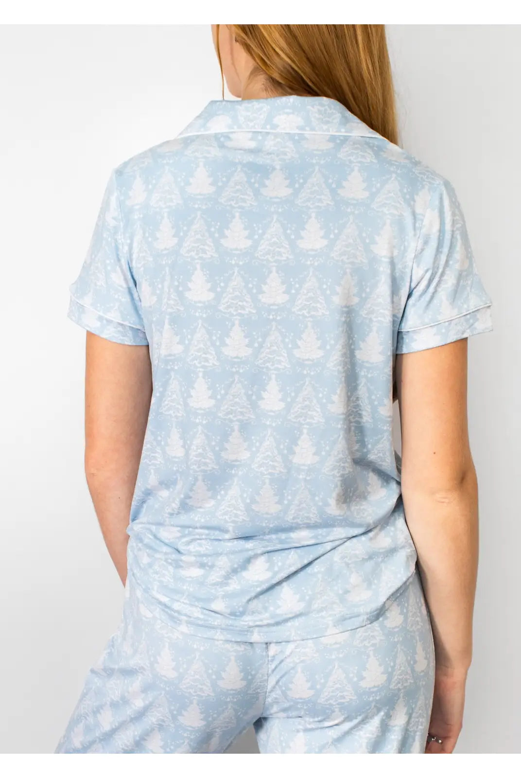 A woman shown from the back wearing a light blue short-sleeve collared top and matching pants with a white tree pattern, against a plain light background.