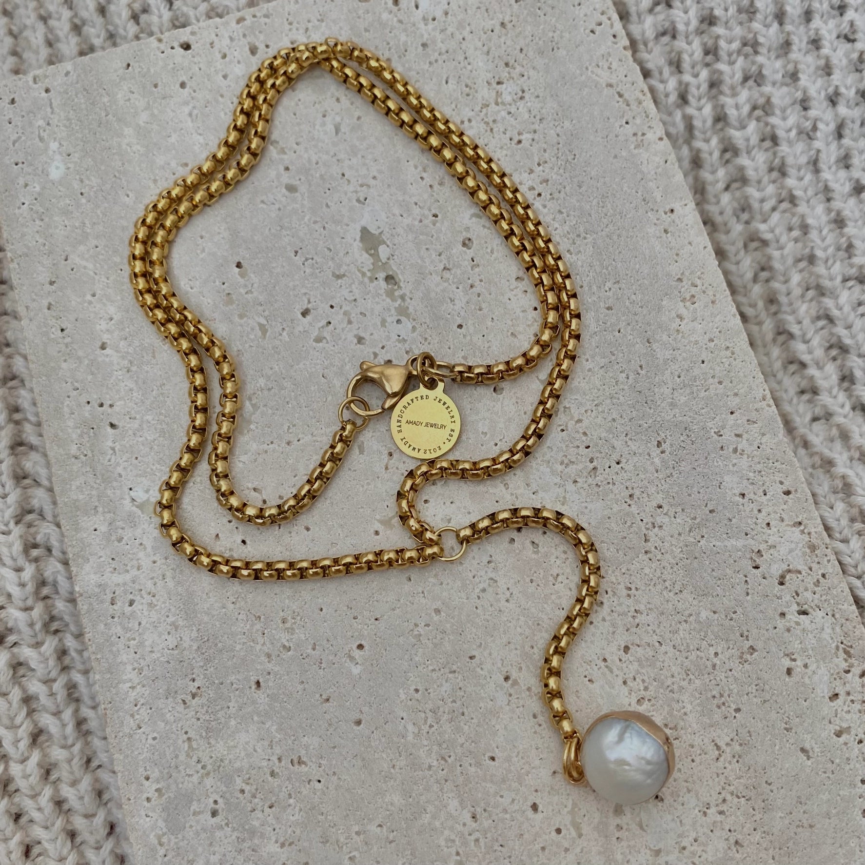 Gold chain necklace with a pearl pendant on a textured surface