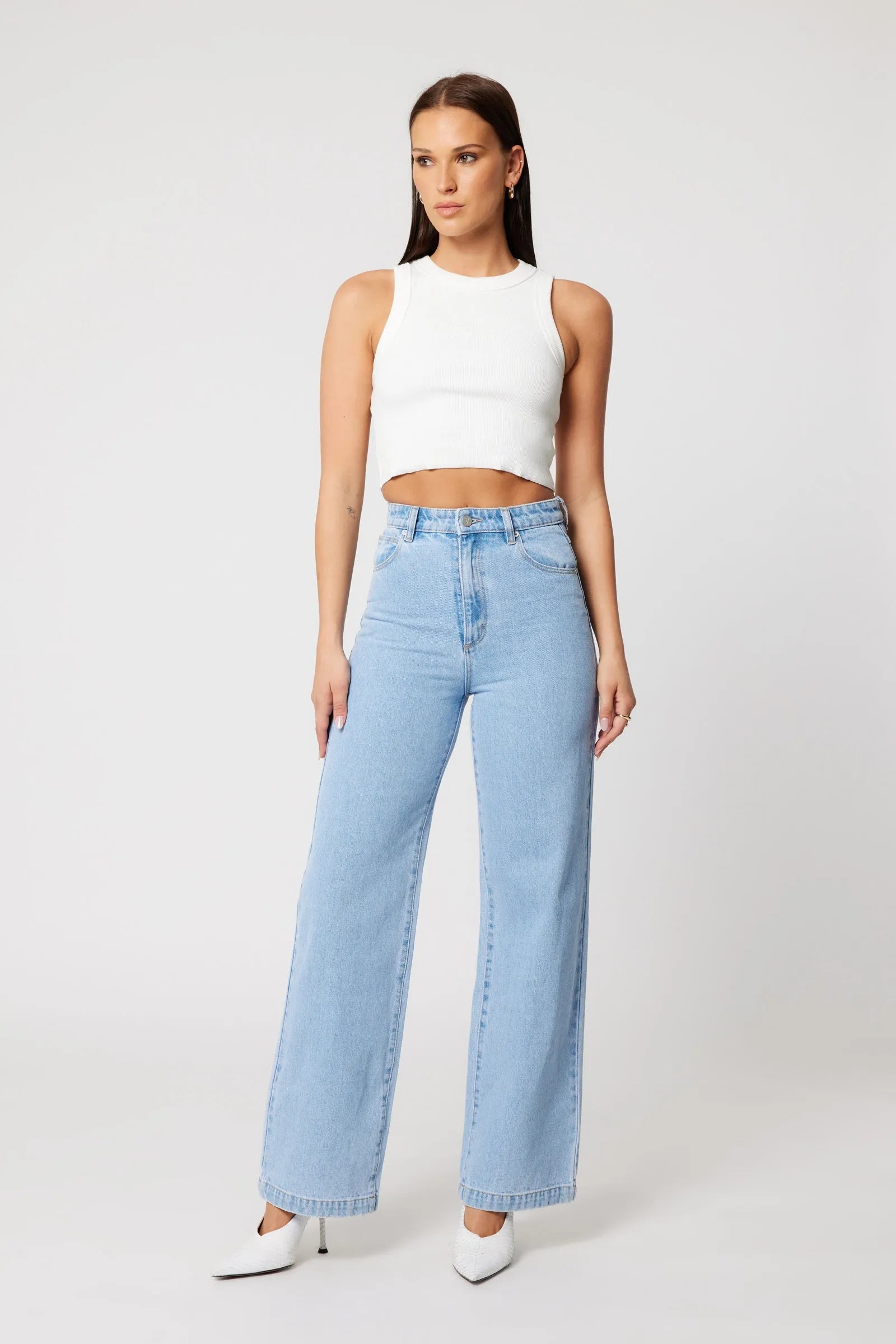 Woman wearing a white sleeveless top and light blue jeans on a white background