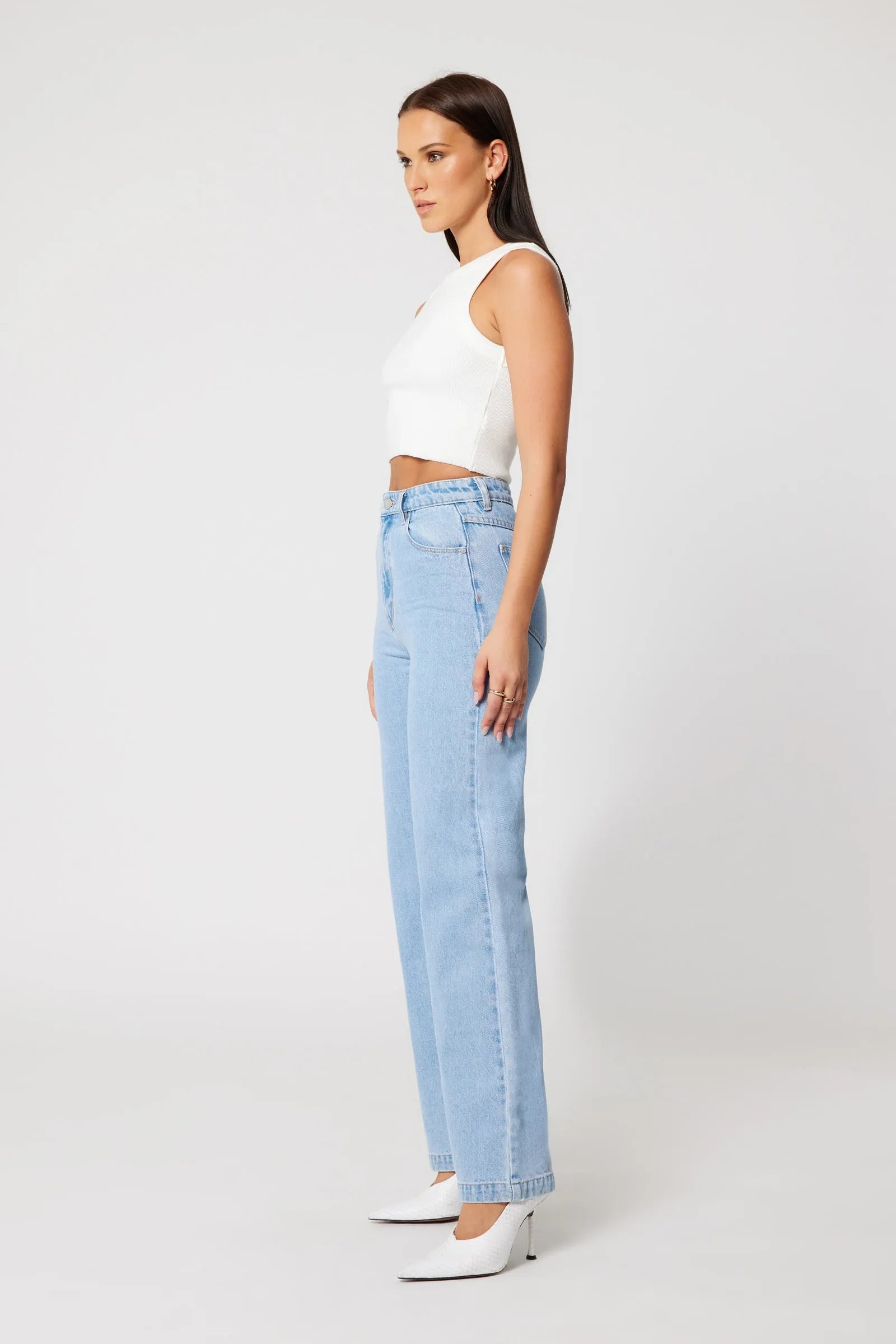 Woman wearing a white sleeveless top and light blue jeans on a white background