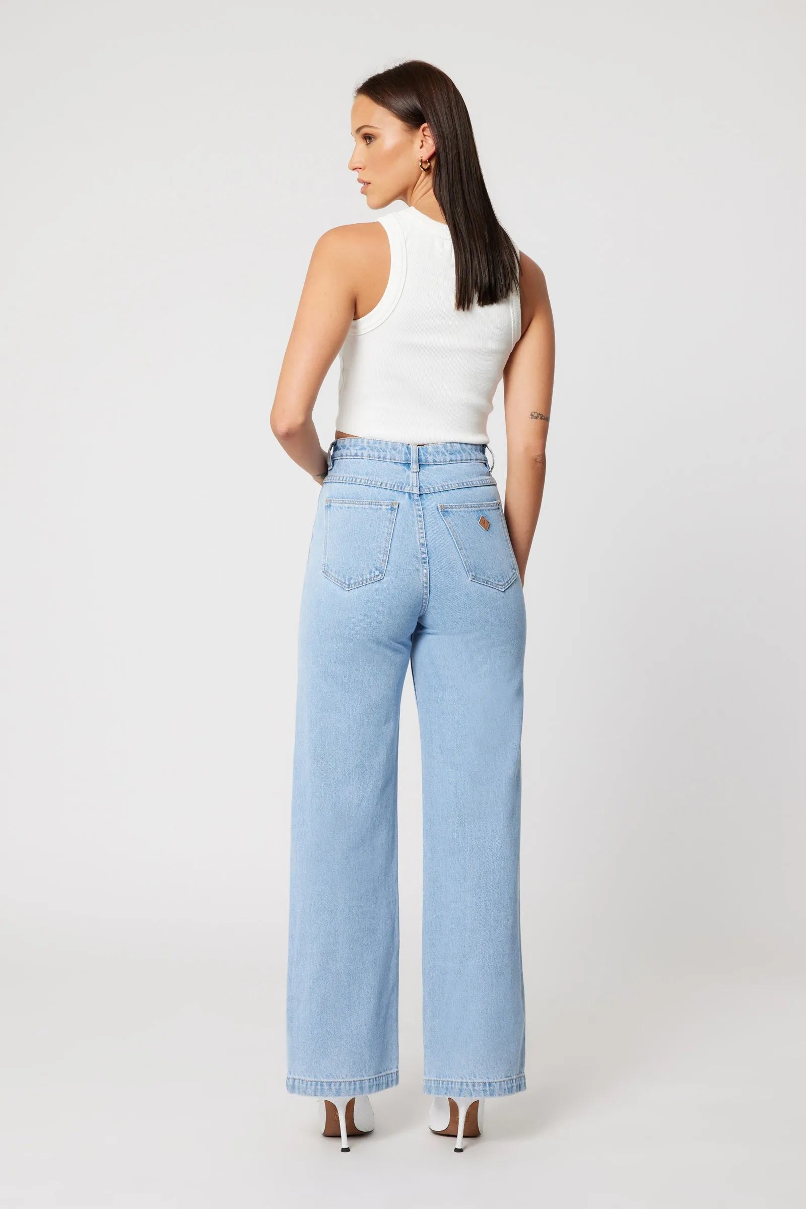 Woman wearing light blue jeans and a white top on a white background