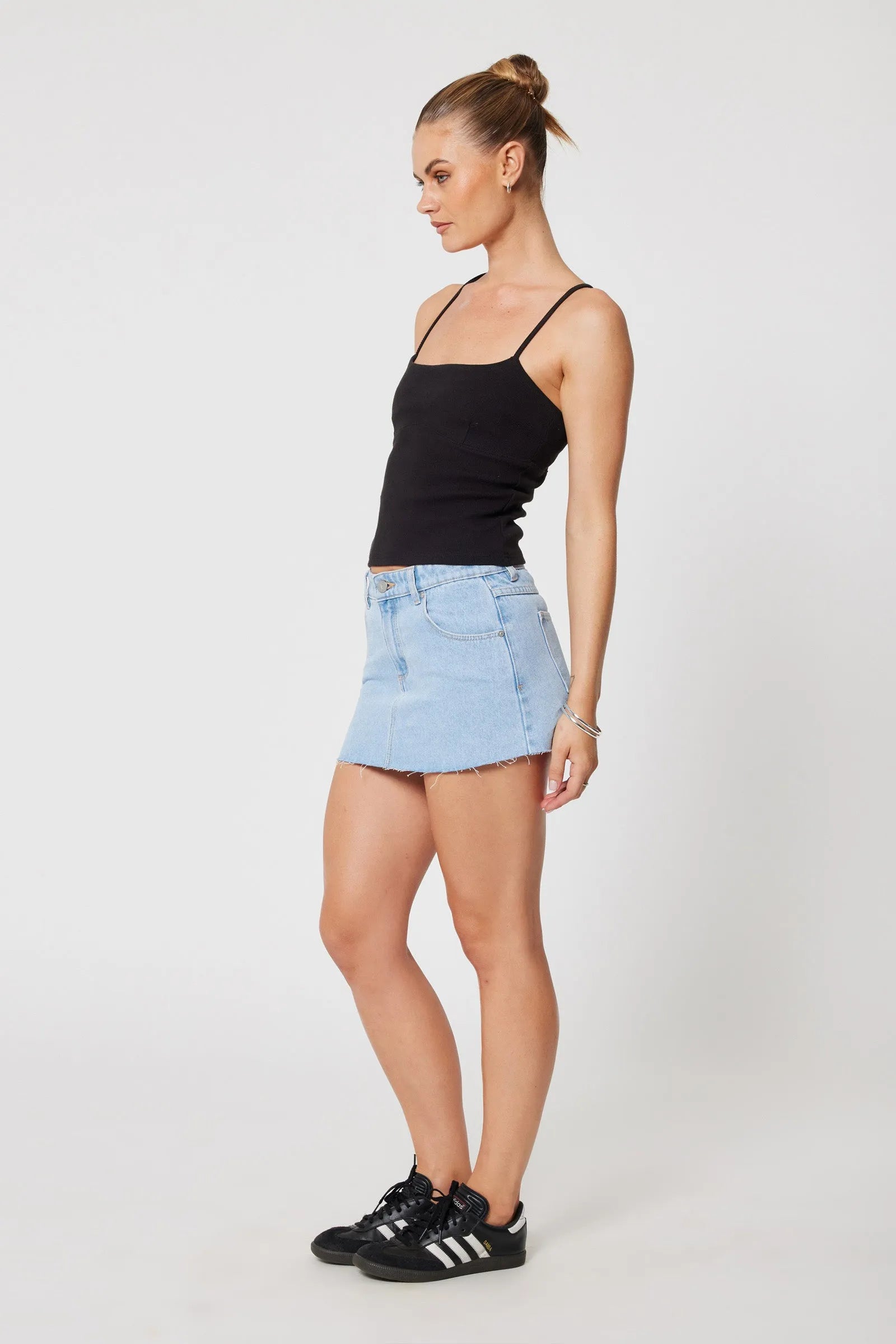 Woman wearing a black tank top and light blue denim skirt on a white background