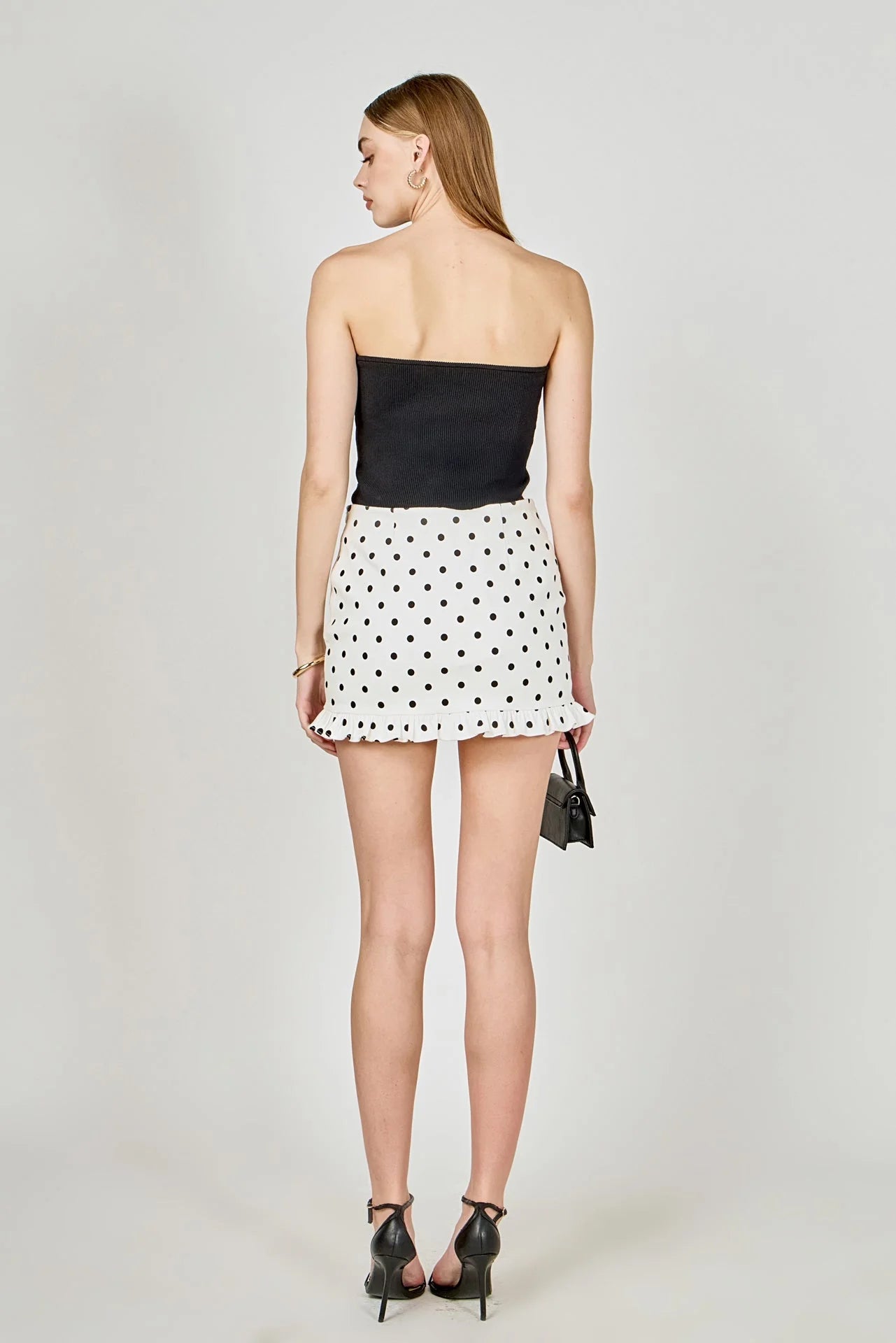 Woman wearing a black strapless top and white polka dot skirt on a plain background