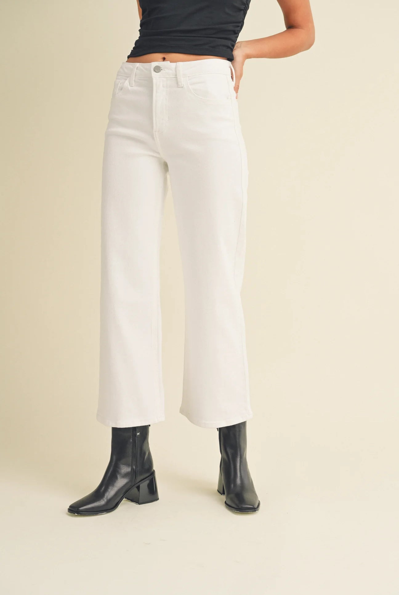 Person wearing white wide-leg jeans and black boots on a beige background