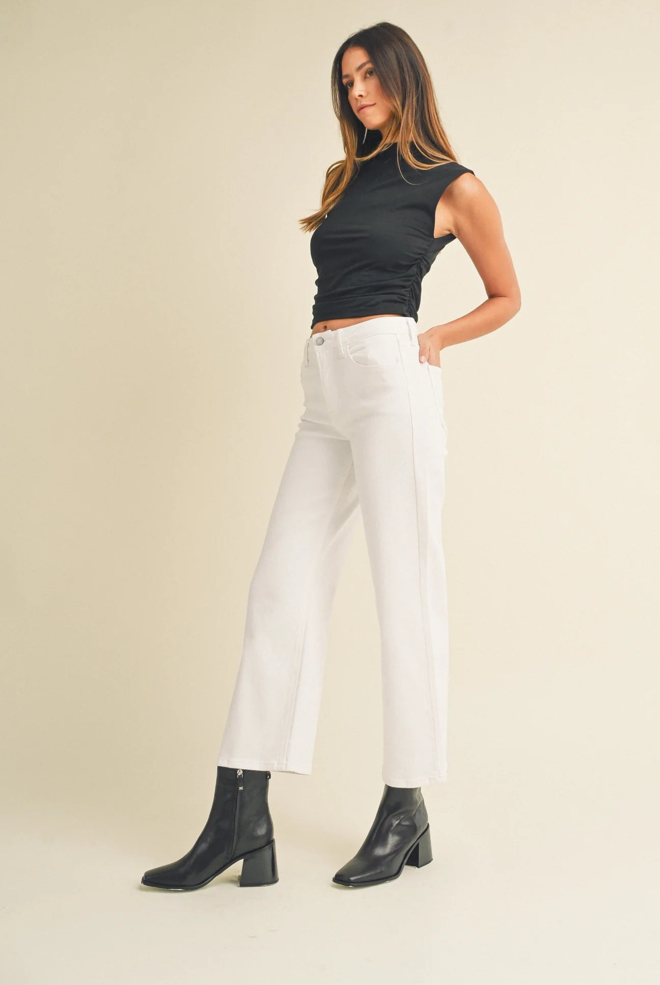 Woman wearing a black top and white pants with black boots on a beige background