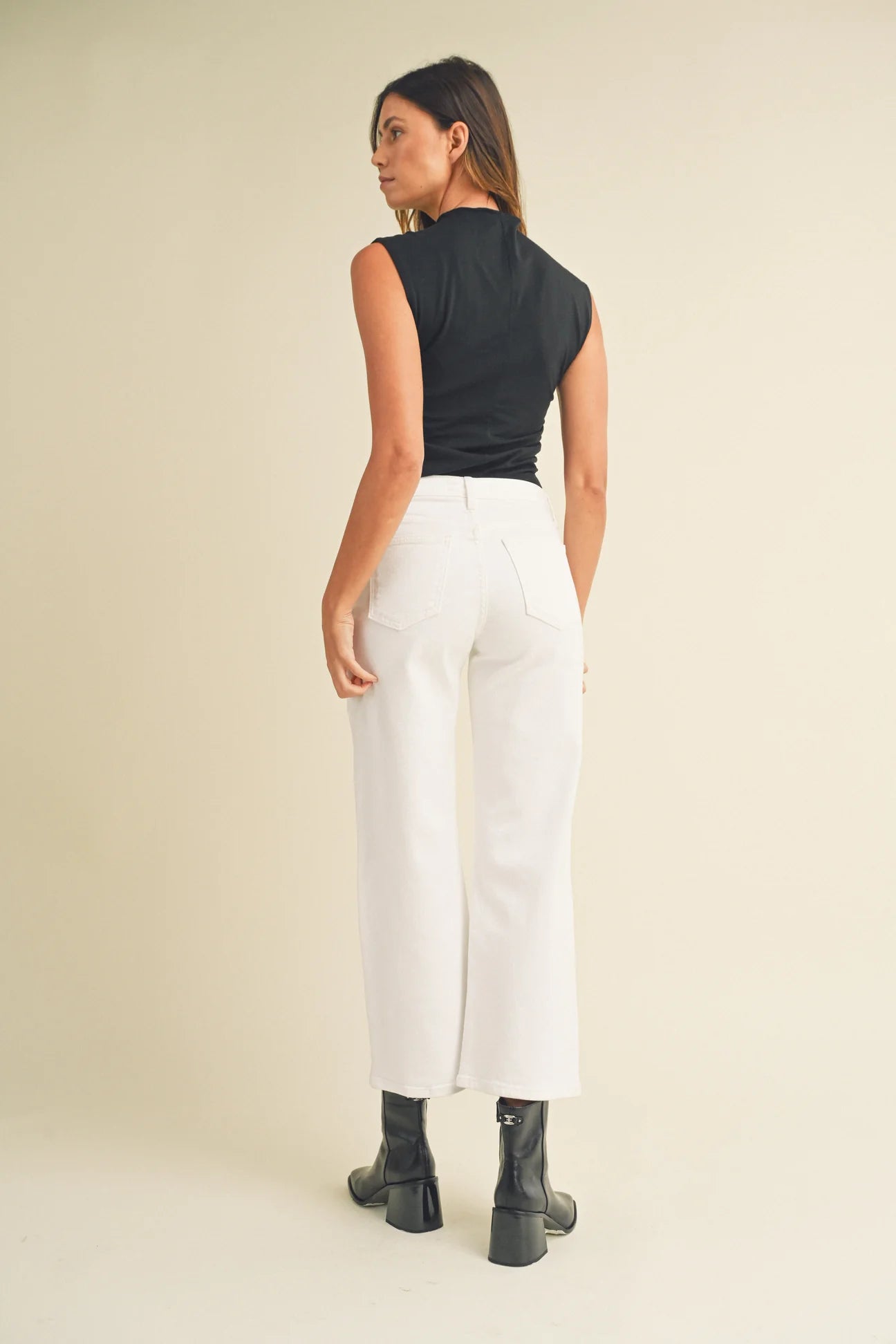 Woman wearing a black sleeveless top and white pants on a beige background