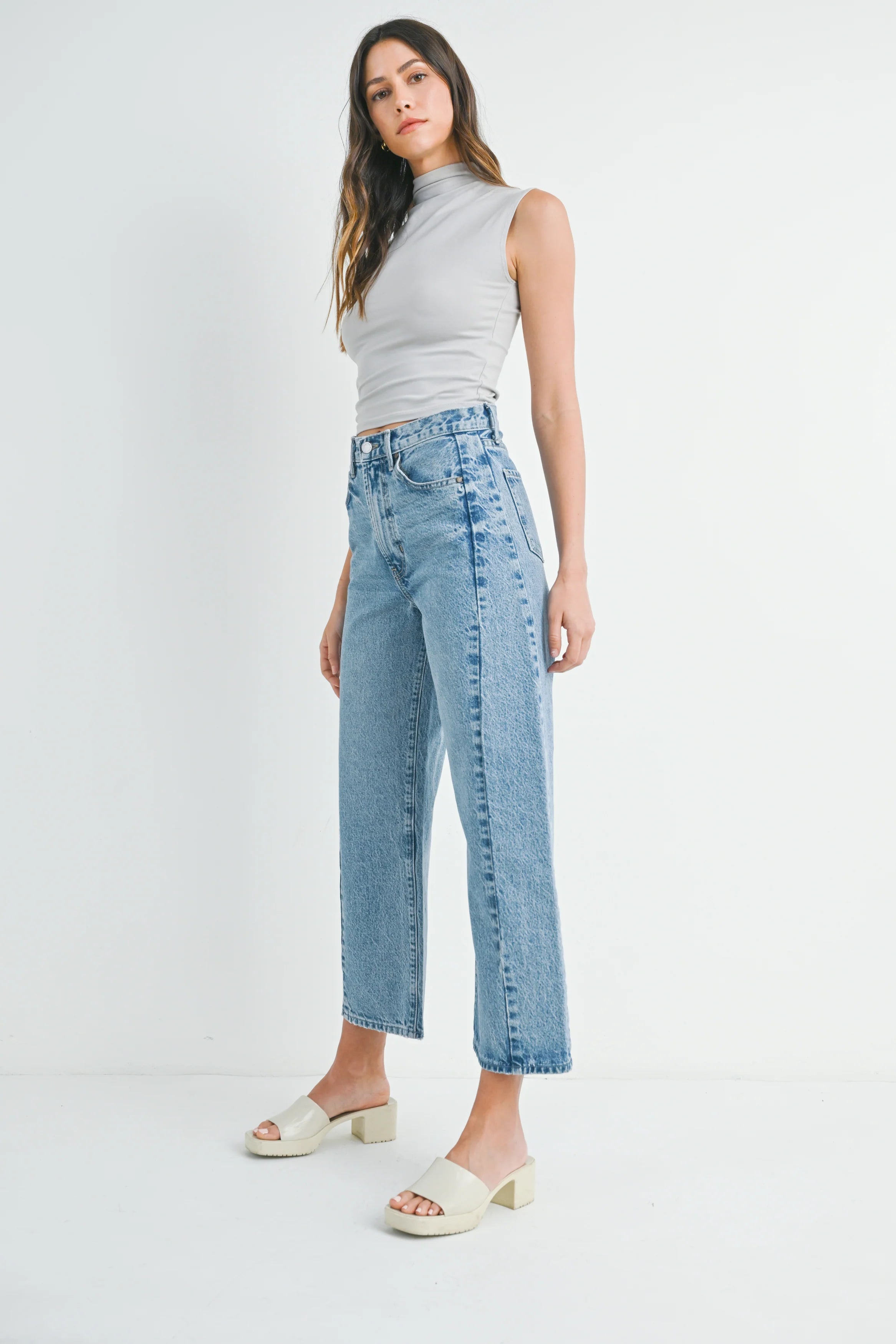 Woman wearing a gray sleeveless top and light blue jeans on a white background
