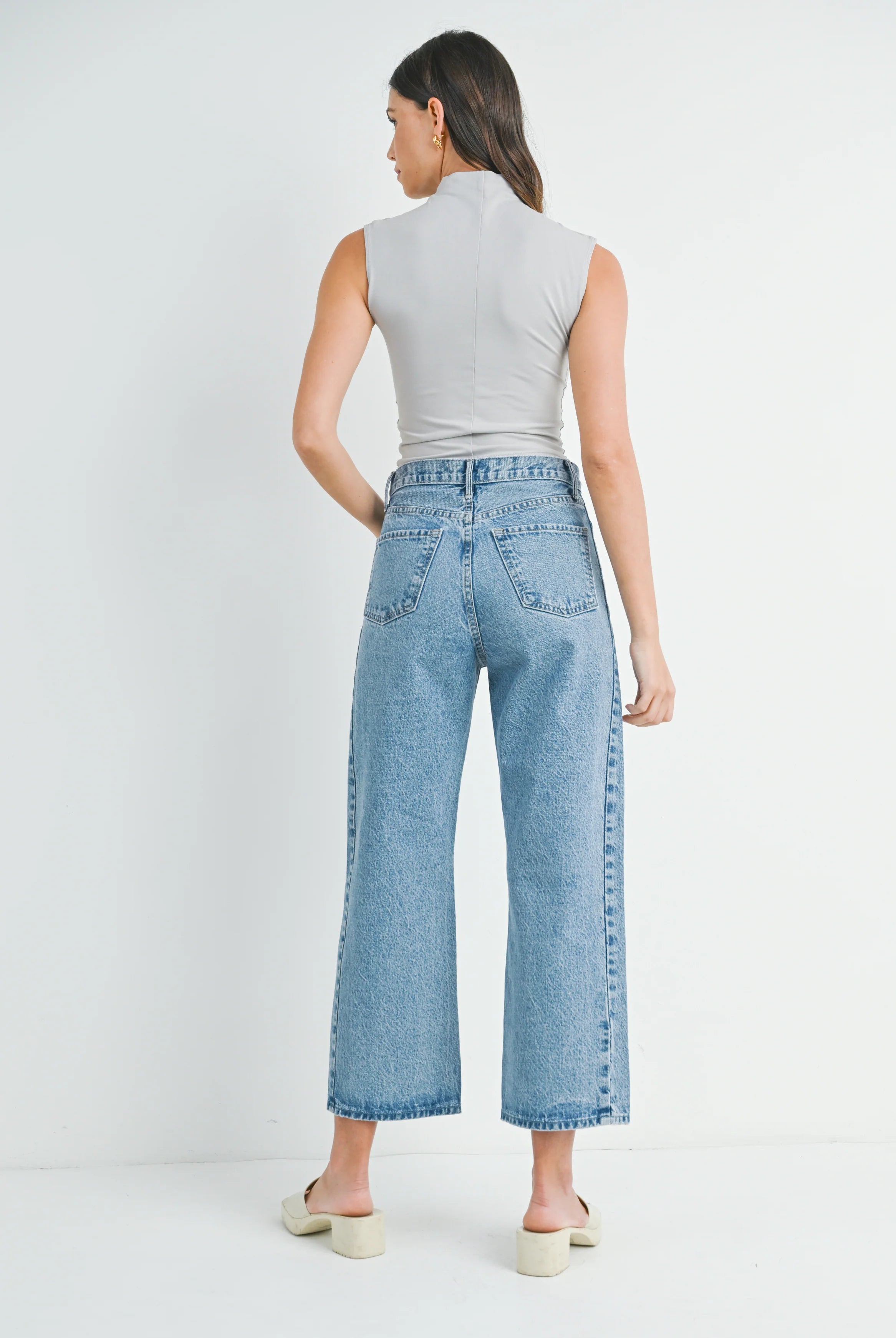Woman wearing light blue jeans and a gray sleeveless top on a white background