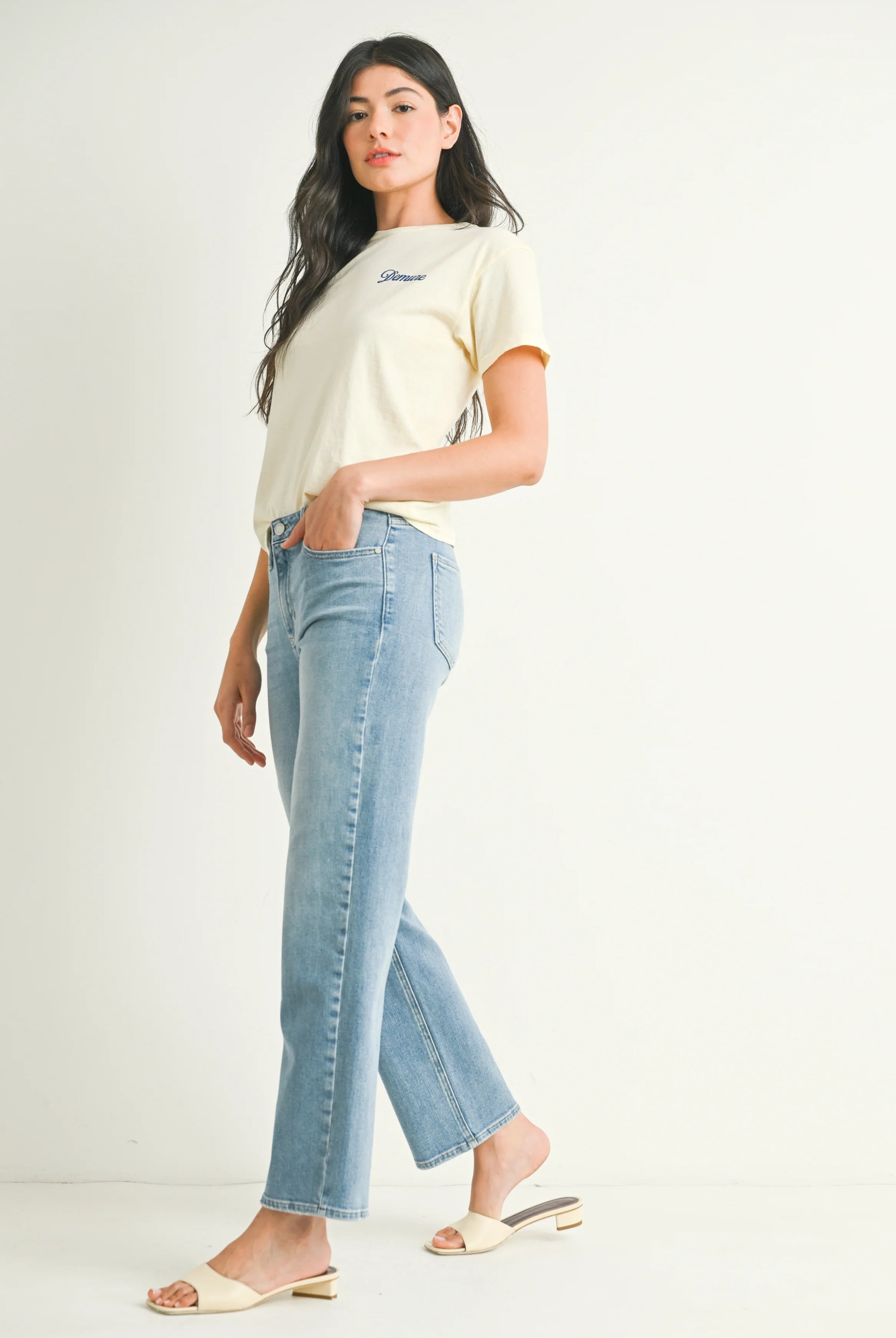 Woman wearing a cream t-shirt and light blue jeans on a white background