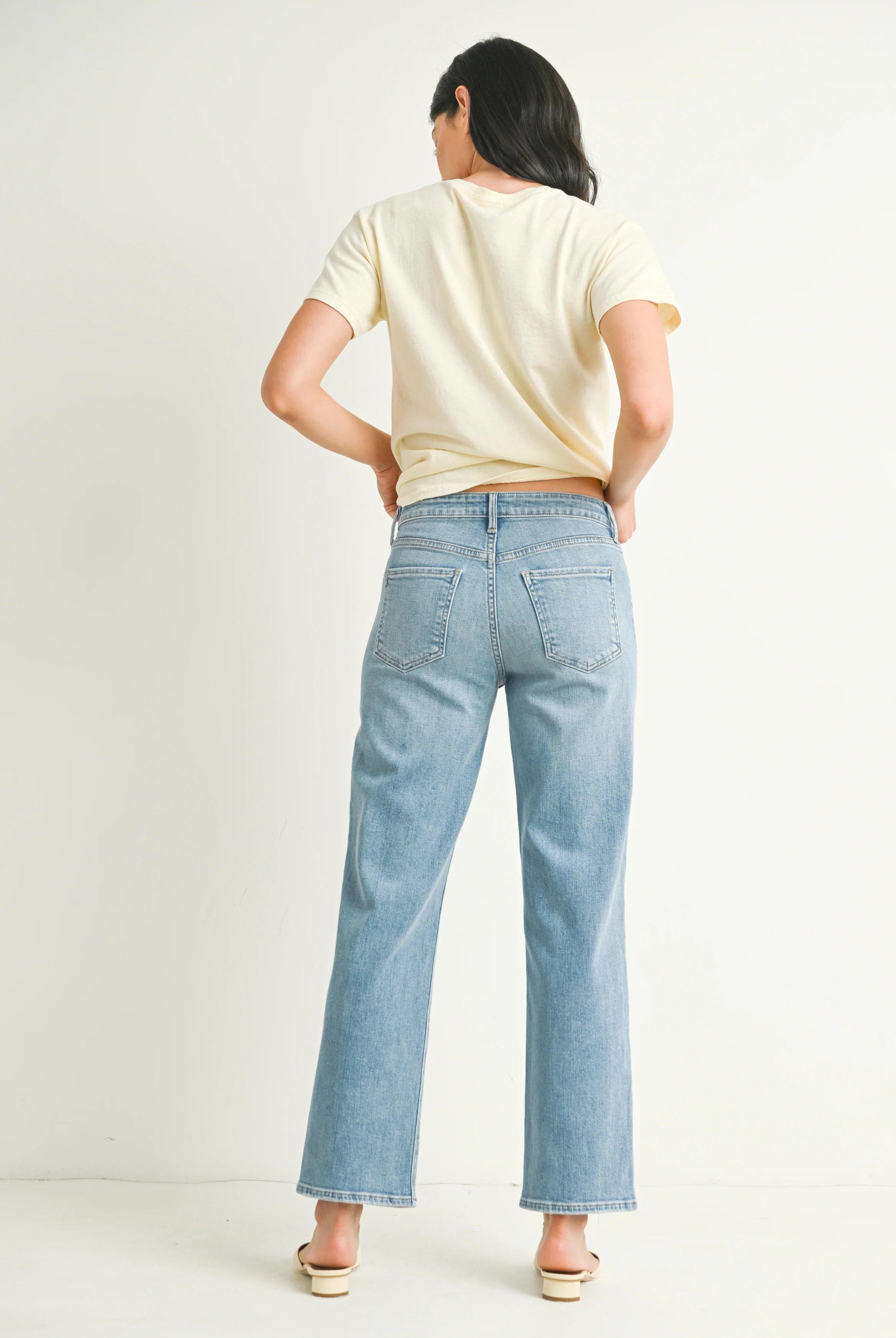 Woman wearing light blue jeans and a beige top on a plain background