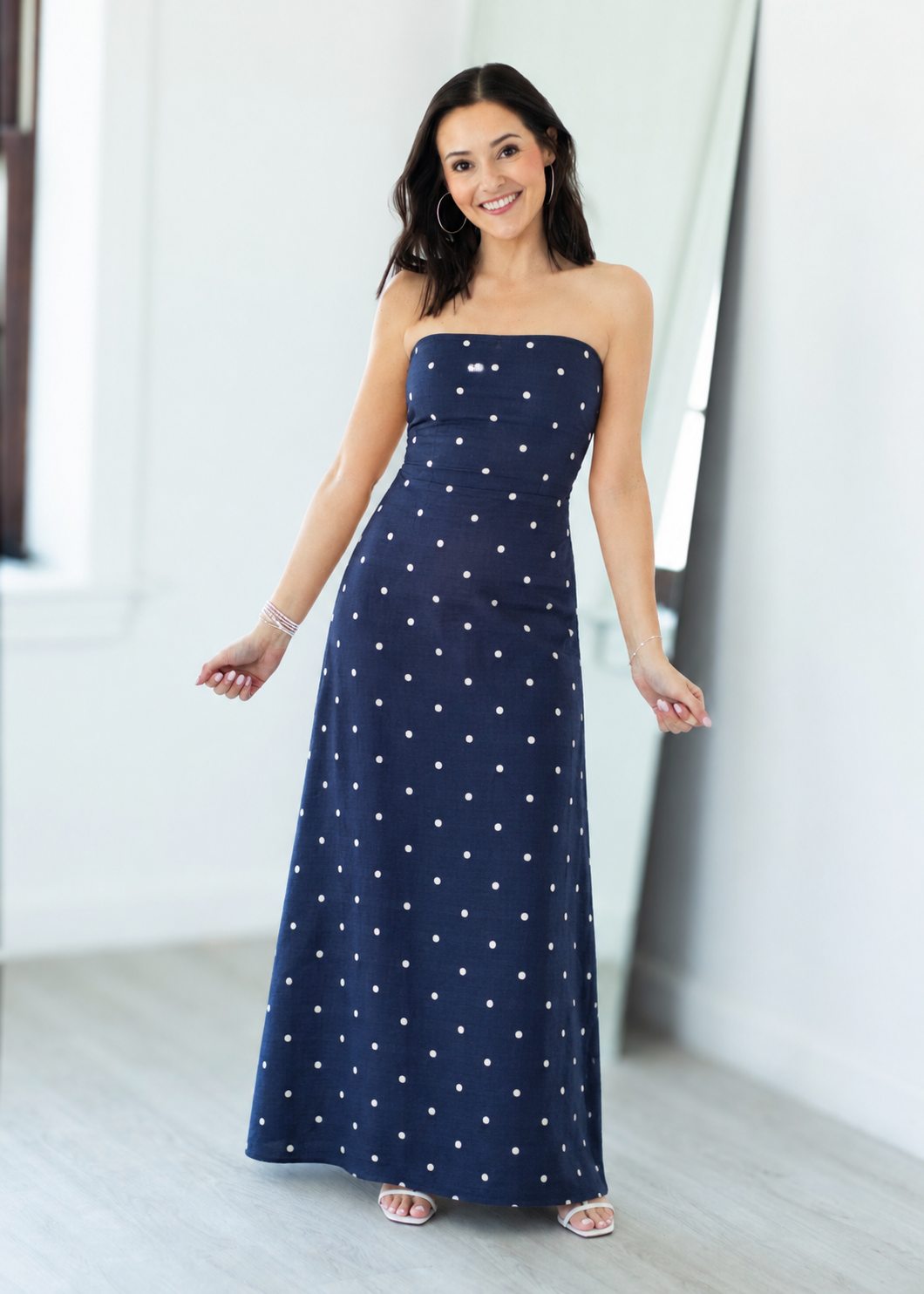 Woman wearing a strapless navy dress with white polka dots in a bright room.