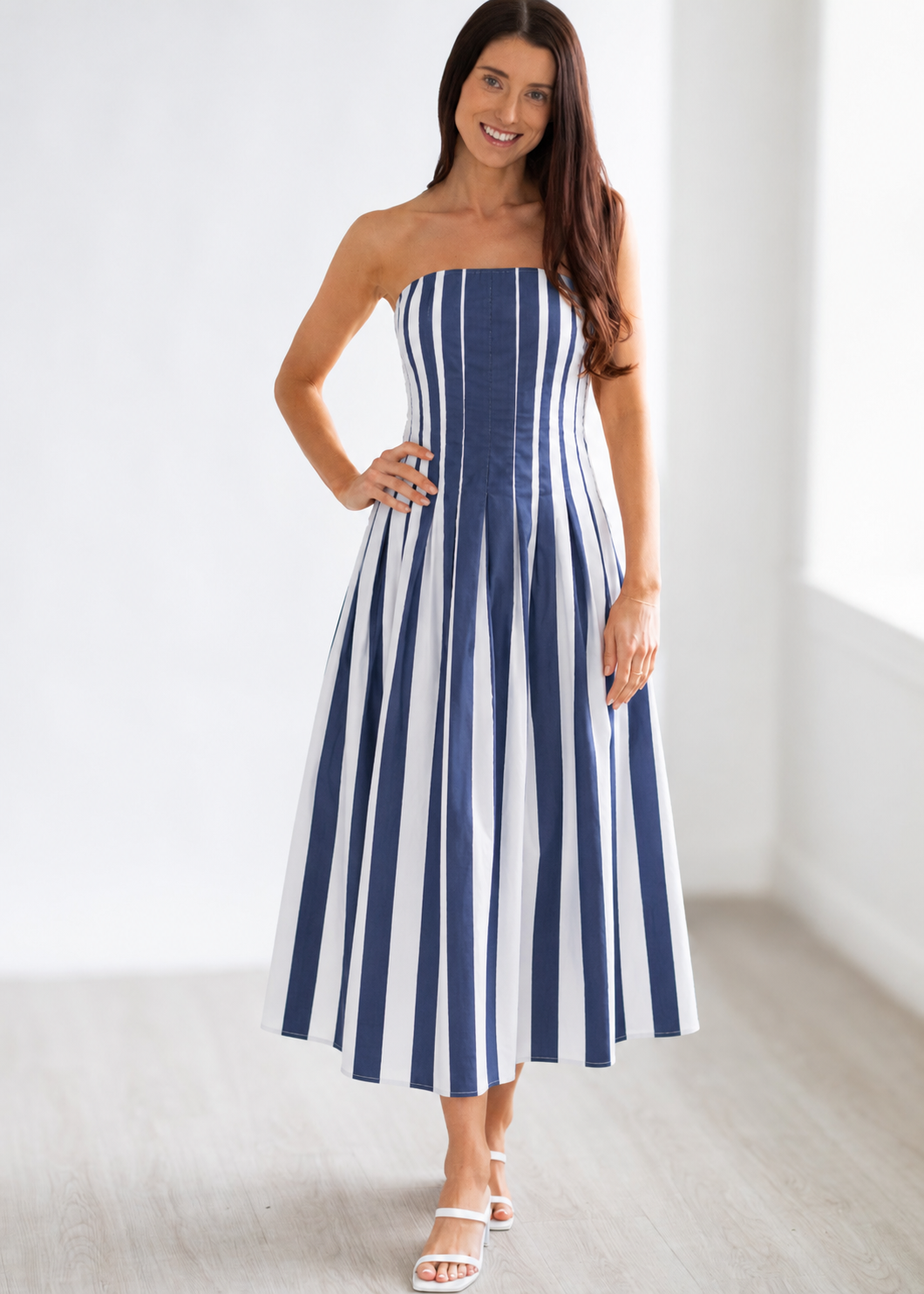 Woman wearing a strapless blue and white striped dress against a white background