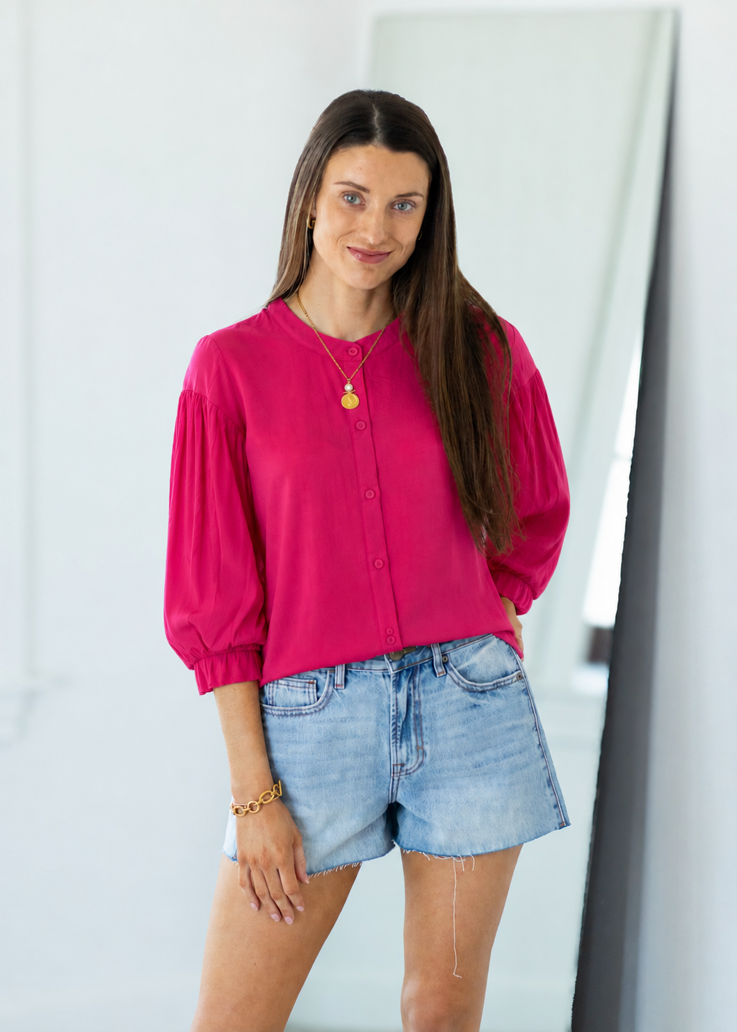 Woman wearing a bright pink blouse and denim shorts against a white background
