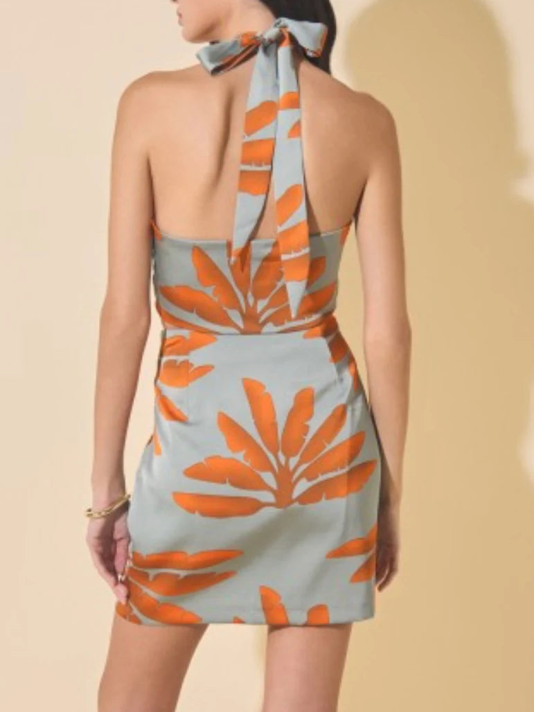 Woman wearing a halter neck dress with orange leaf pattern on a beige background