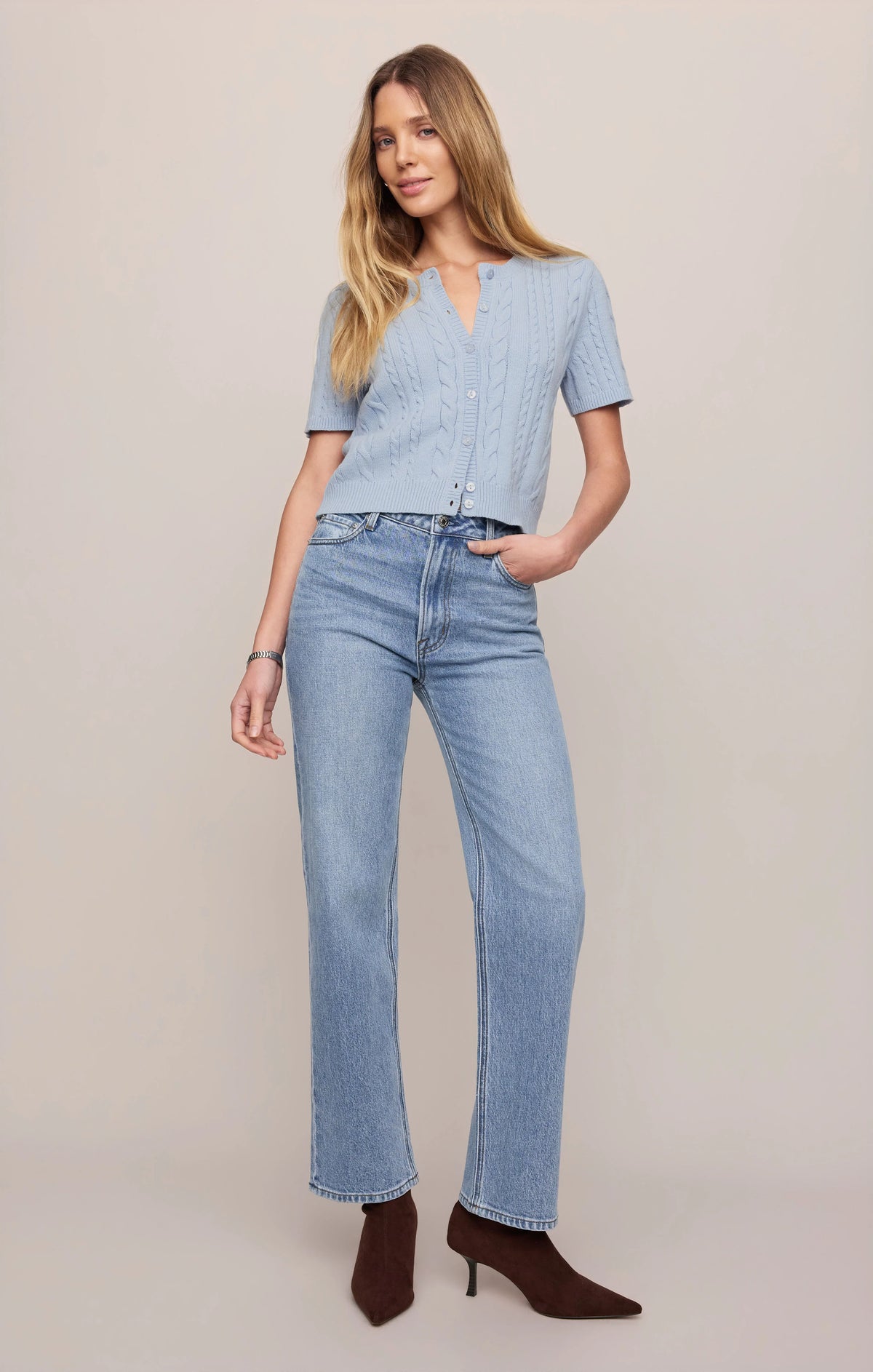 Woman wearing a light blue top and jeans on a plain background