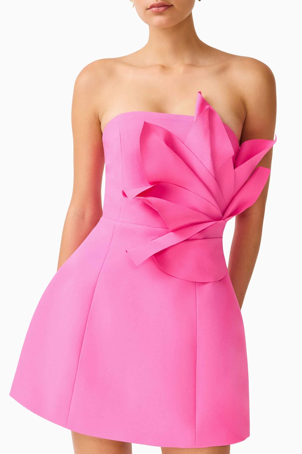 A bright pink strapless mini dress with a large sculptural layered bow detail on the bodice, shown on a model against a plain white background.