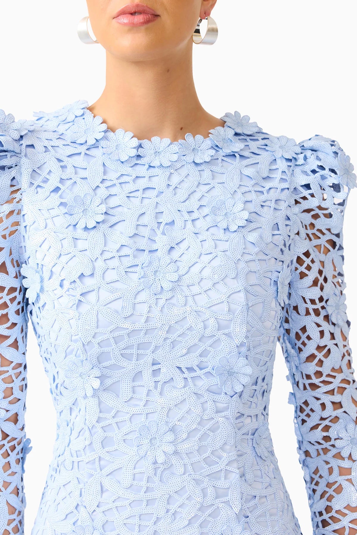 A close-up of a model wearing a light blue lace dress with long sheer sleeves and a high neckline.