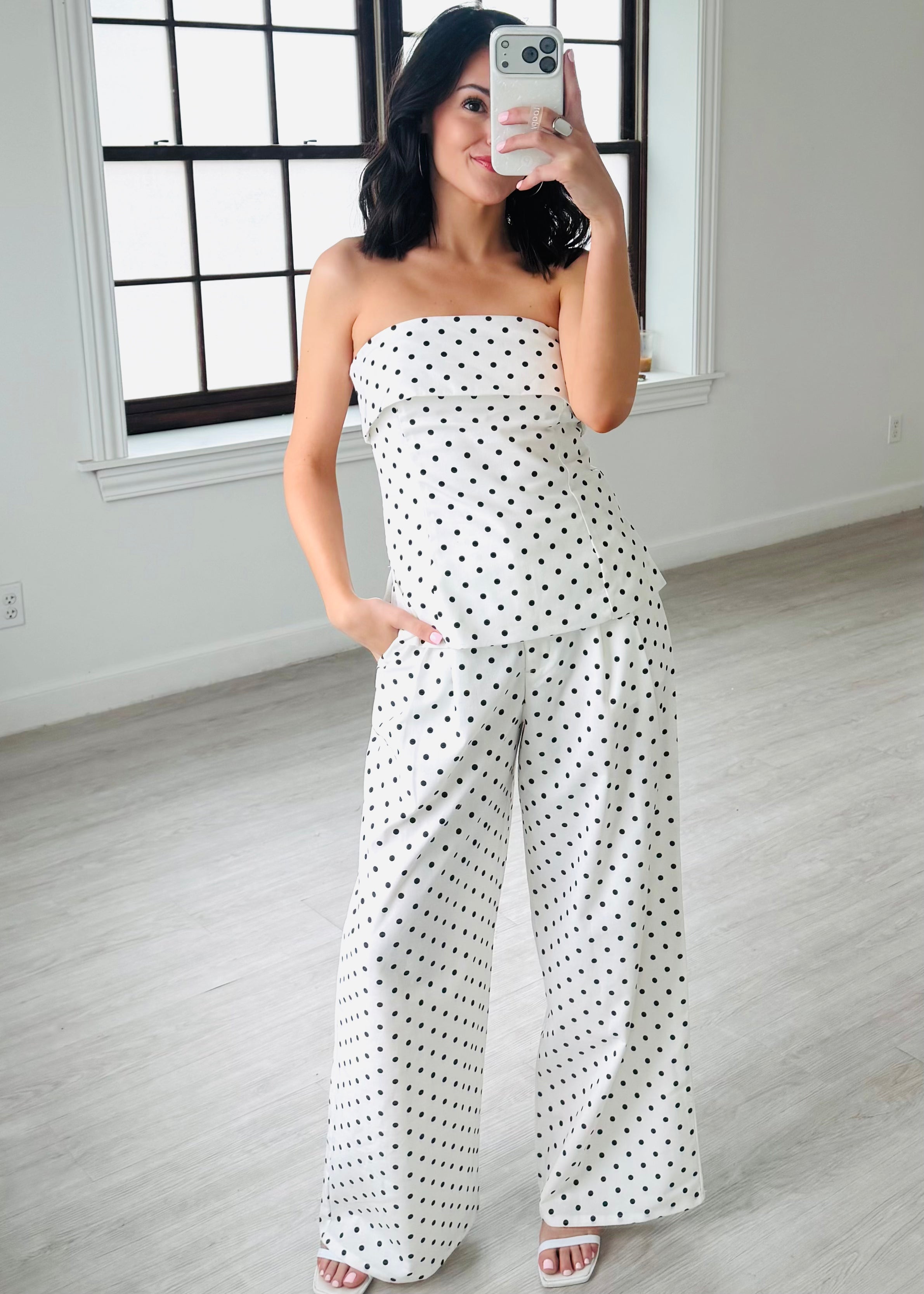 Woman wearing a strapless polka dot jumpsuit in a minimalistic room.