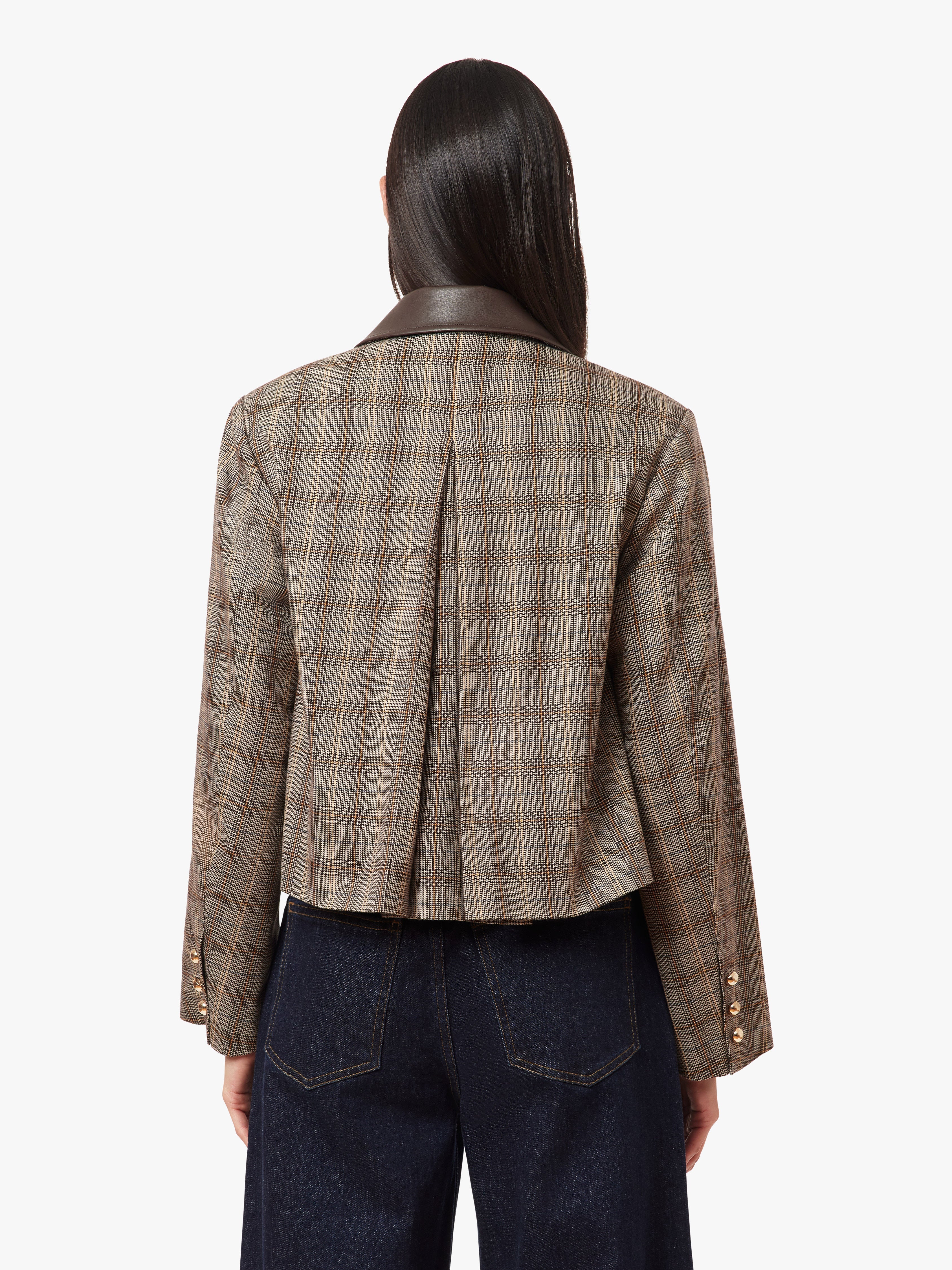 A model shown from the back wearing a cropped plaid blazer with a dark brown leather collar, paired with dark blue jeans, against a plain white background.