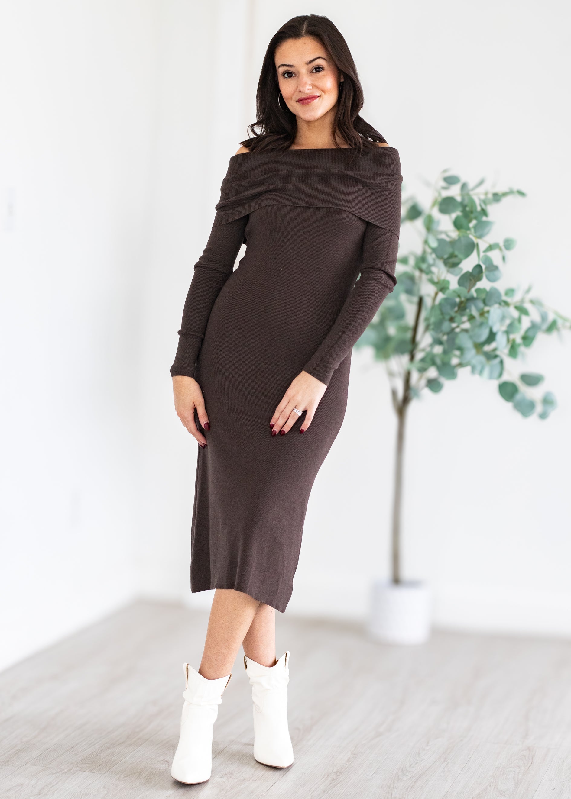 Woman wearing a brown off-shoulder dress with white boots in a minimalistic setting.