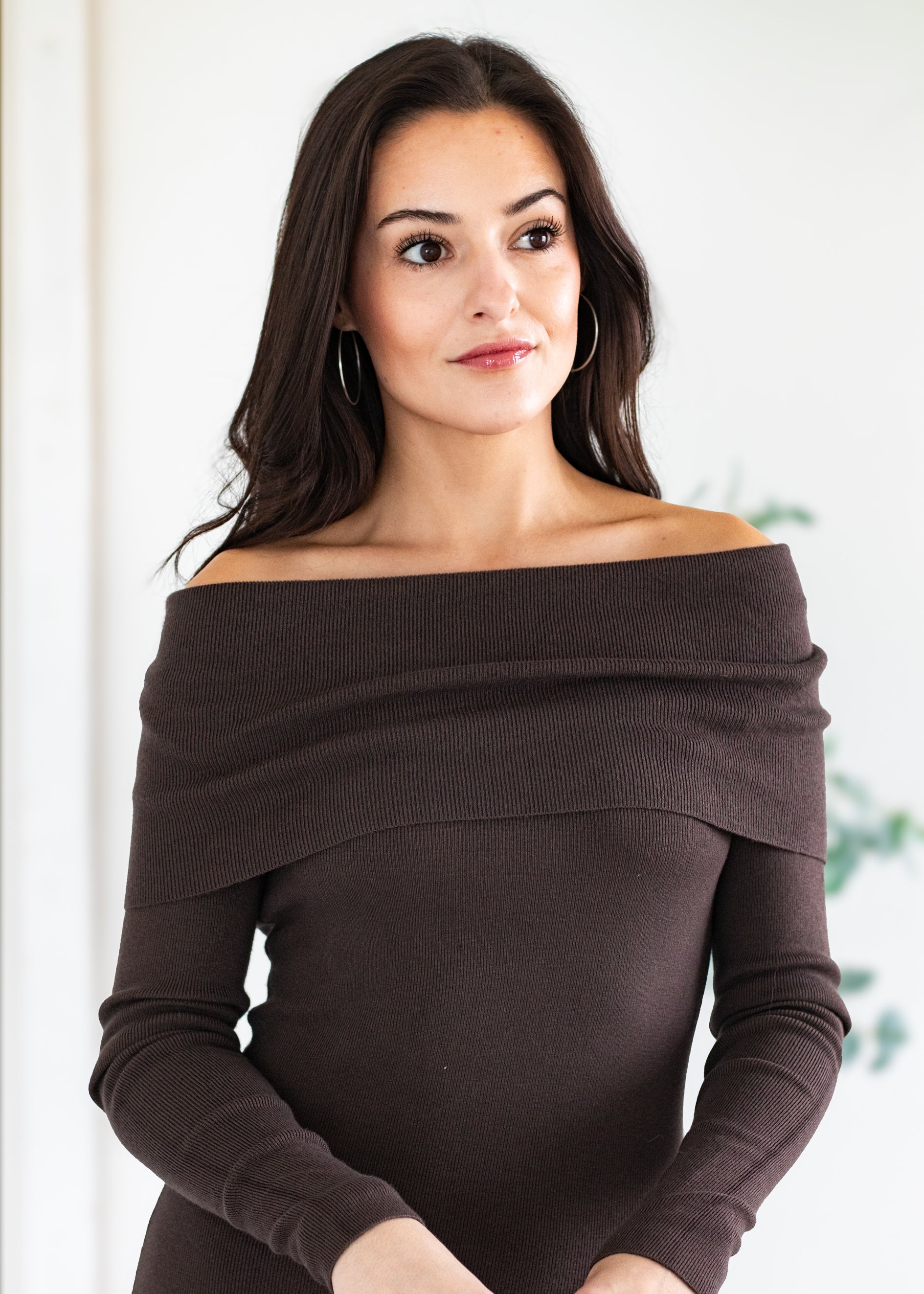 Woman wearing a brown off-shoulder sweater against a white background